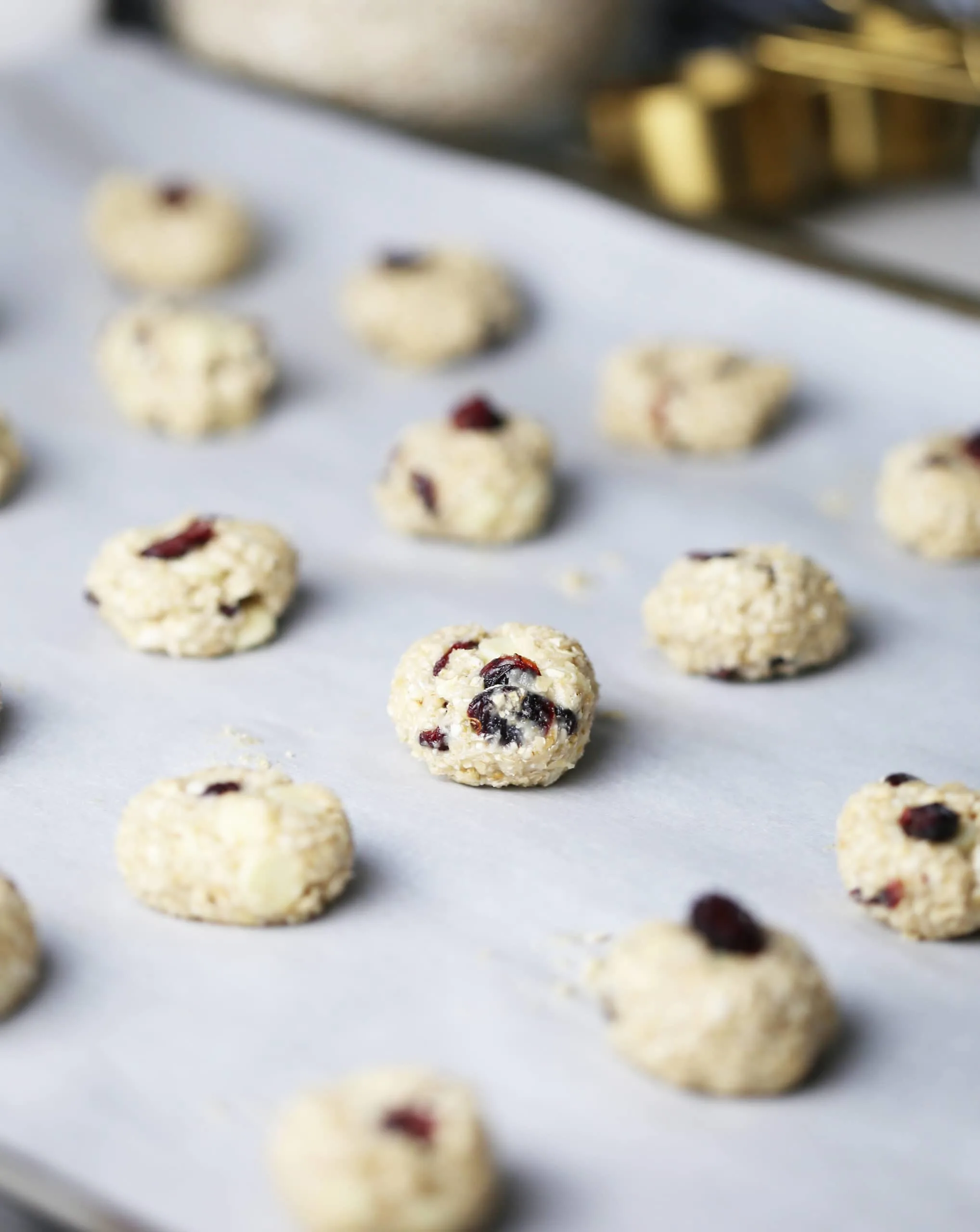 Tablespoon raw white chocolate cranberry oatmeal cookie dough placed on a parchment paper lined baking sheet.