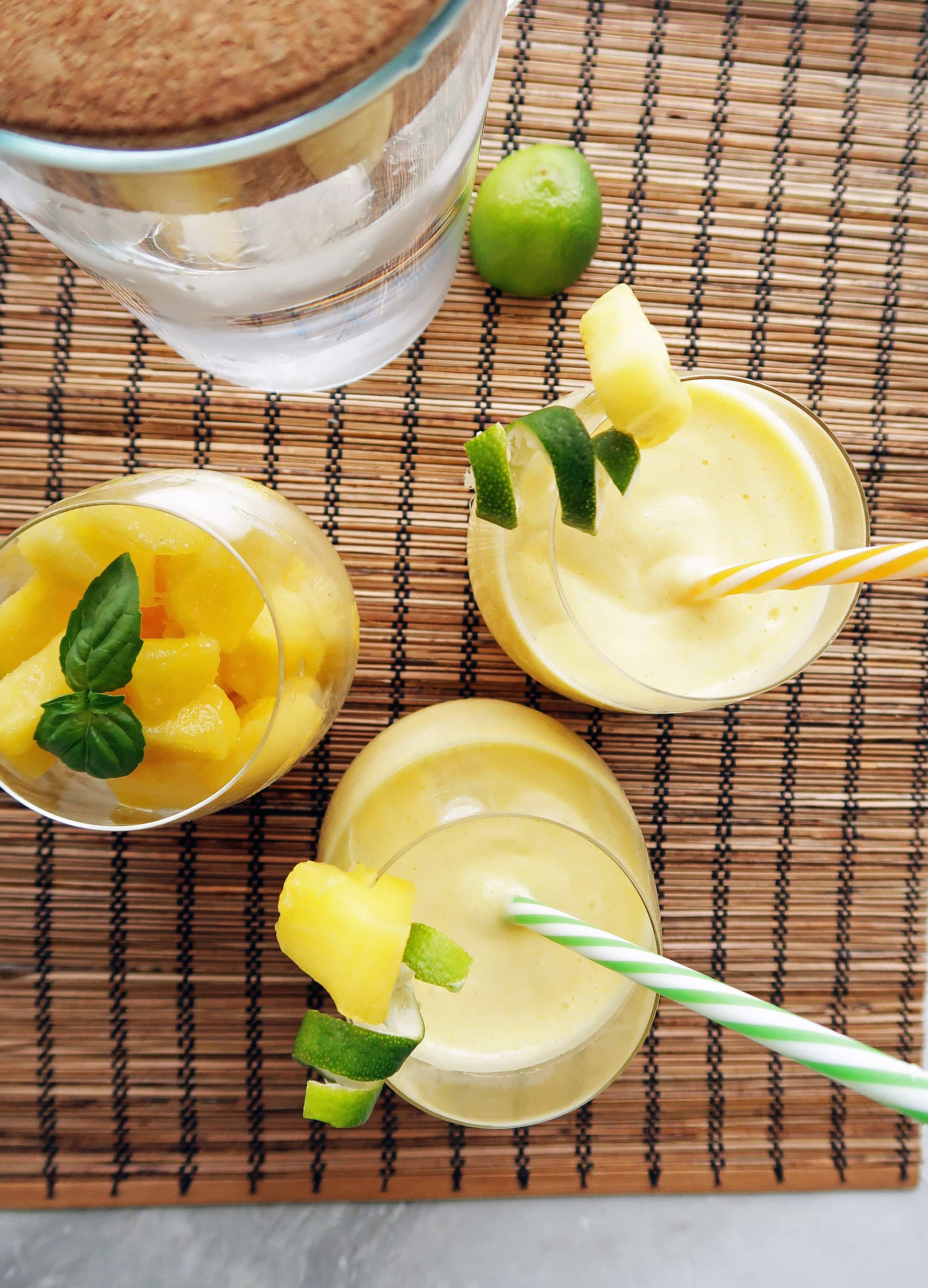 Overhead view of Pineapple Coconut Water Slushies in two glasses, pinepple slices in another glass, and a container of water.