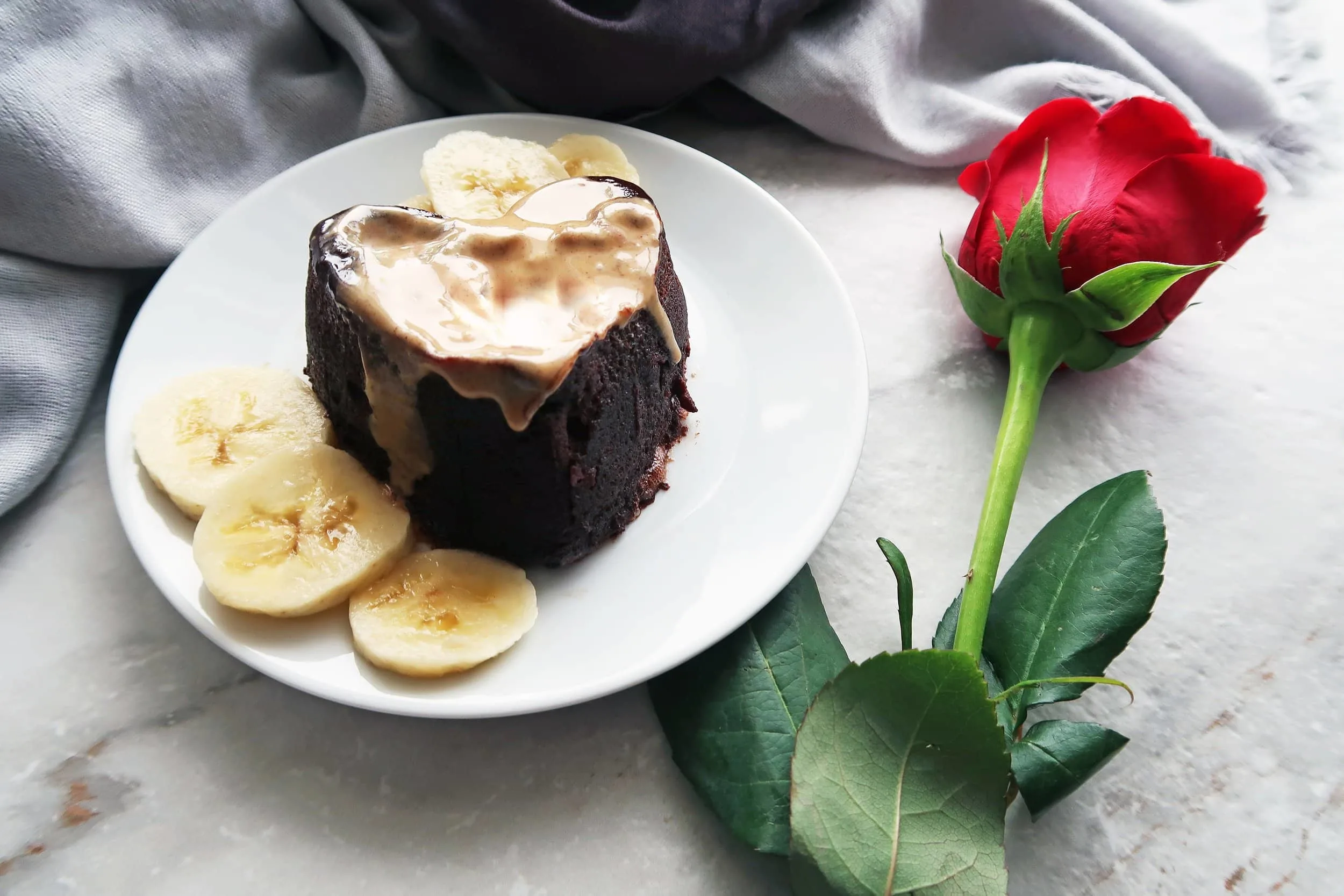 A peanut butter banana chocolate mini cake on a plate next to a rose.