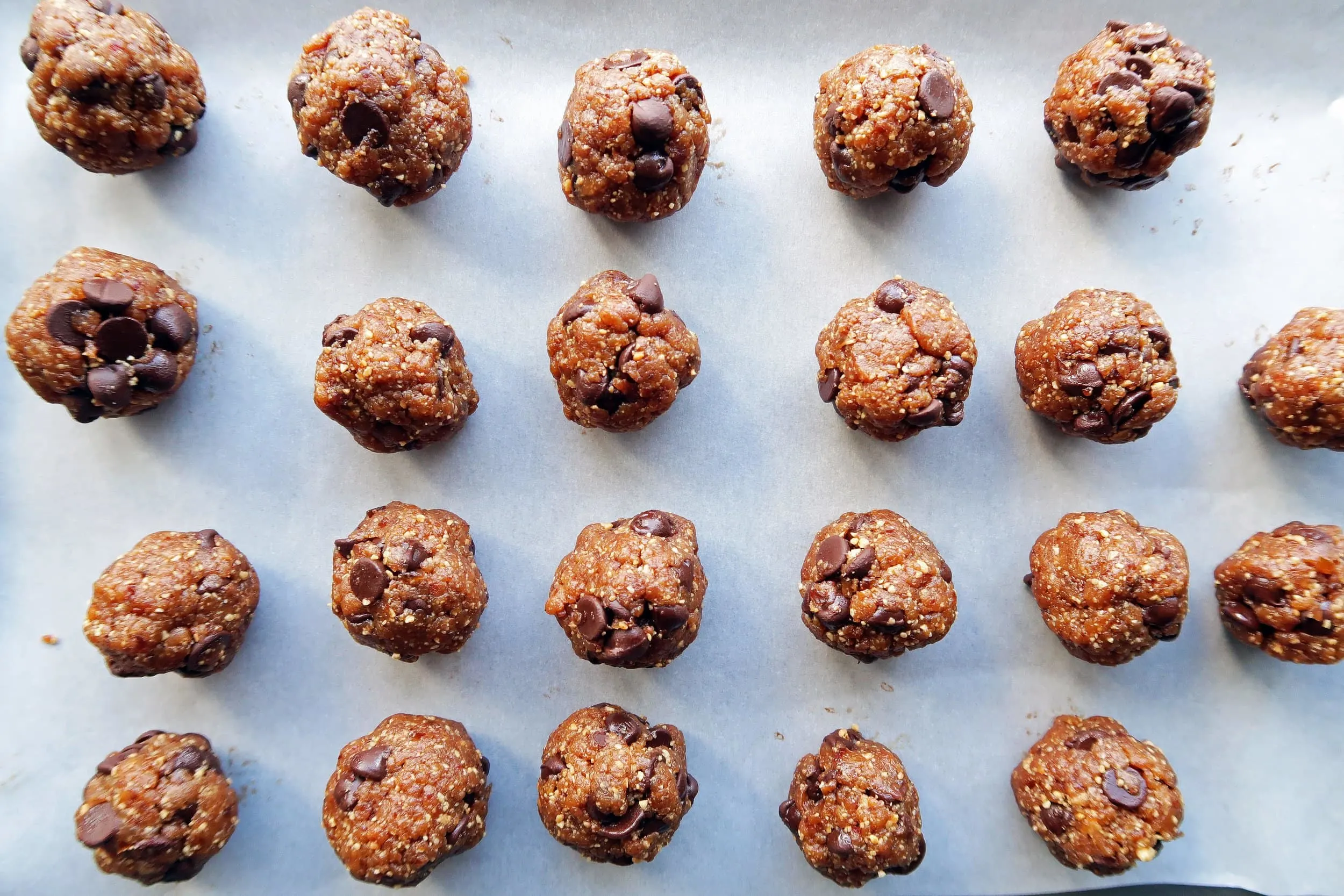 Twenty-two one-inch peanut chocolate chip energy balls on a baking sheet.
