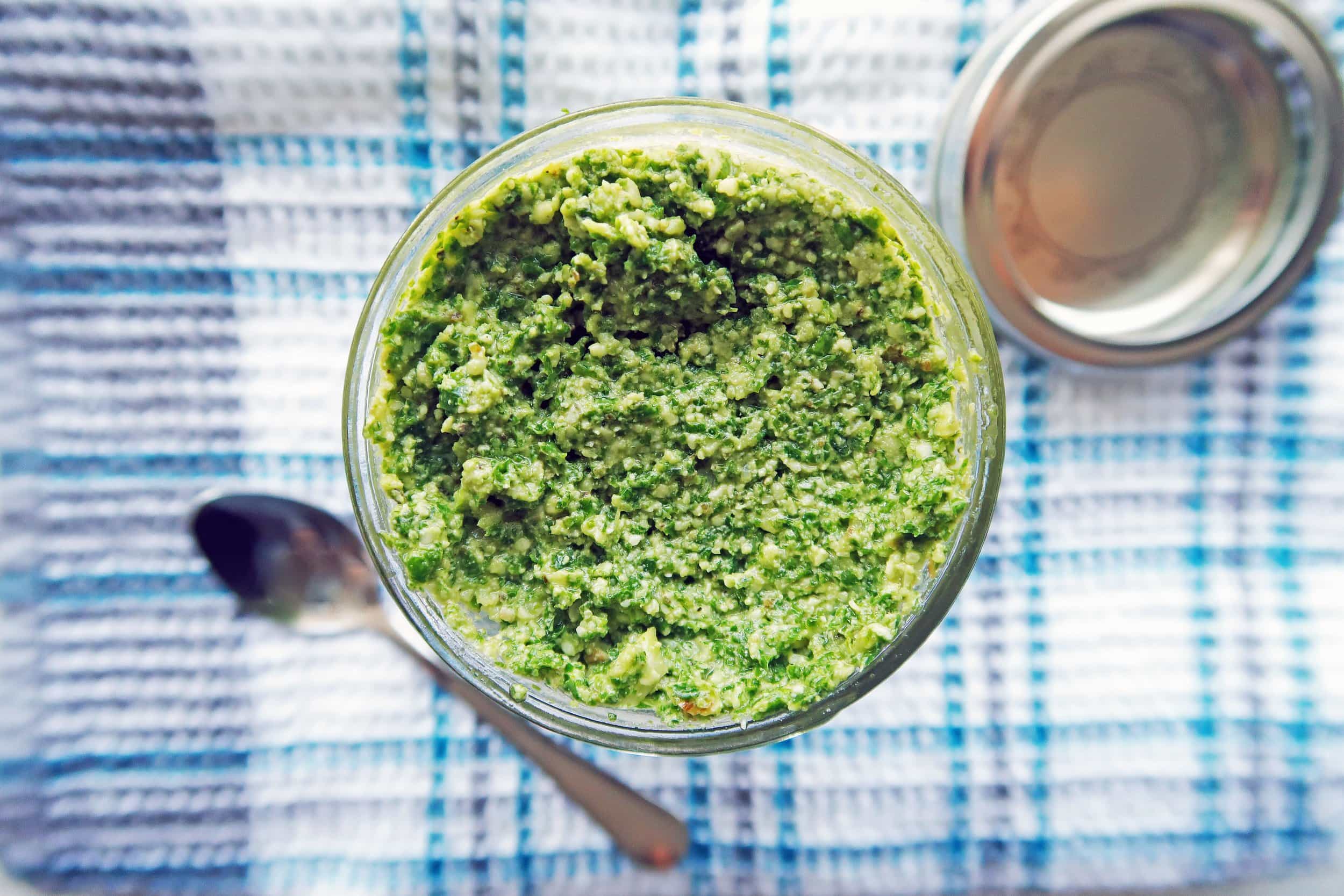 Overhead view of 5 Minute Kale Walnut Pesto in a mason jar; a small spoon to its side.