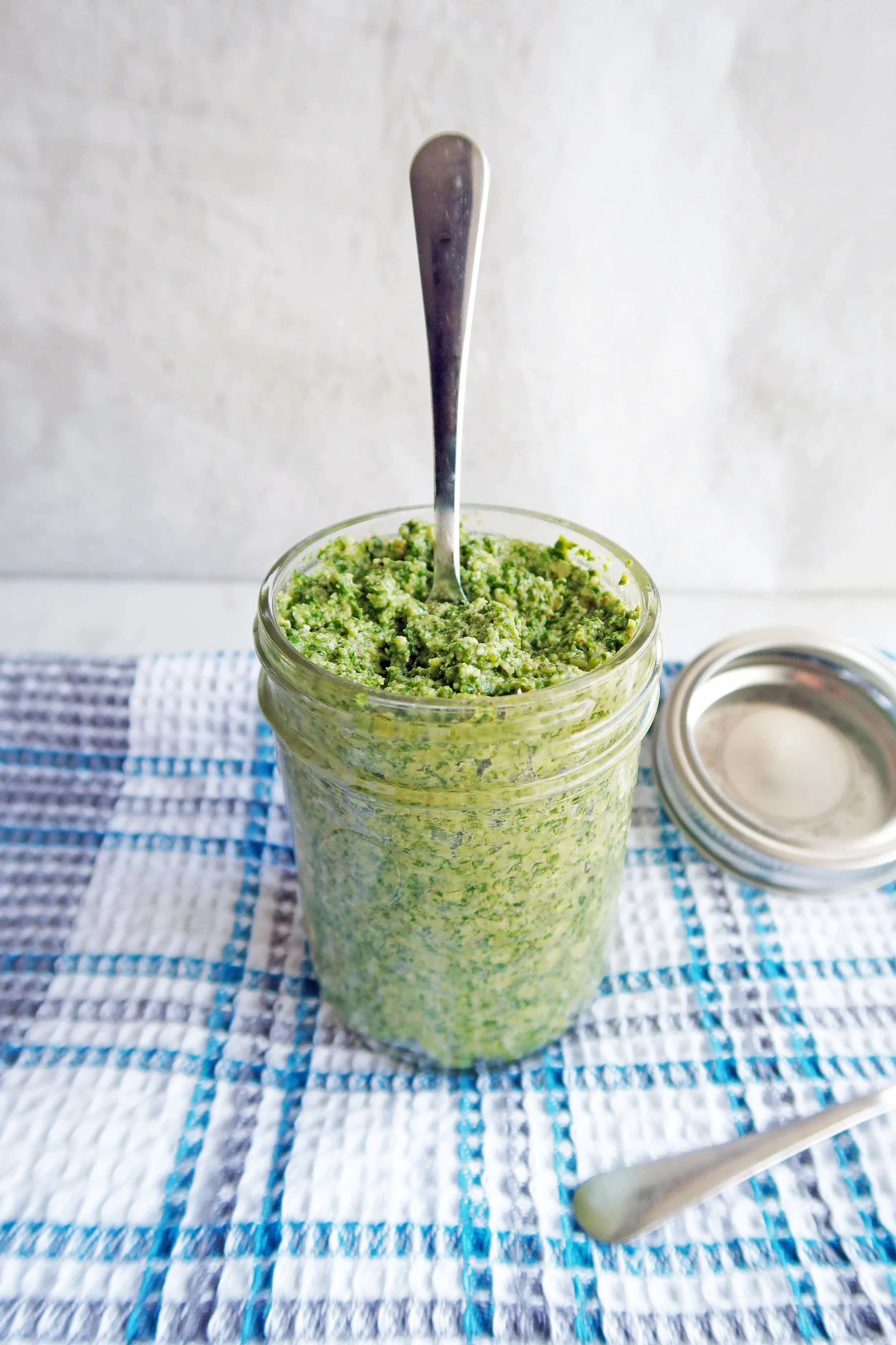 5 Minute Kale Walnut Pesto in a tall mason jar with a spoon sticking upright in the pesto.