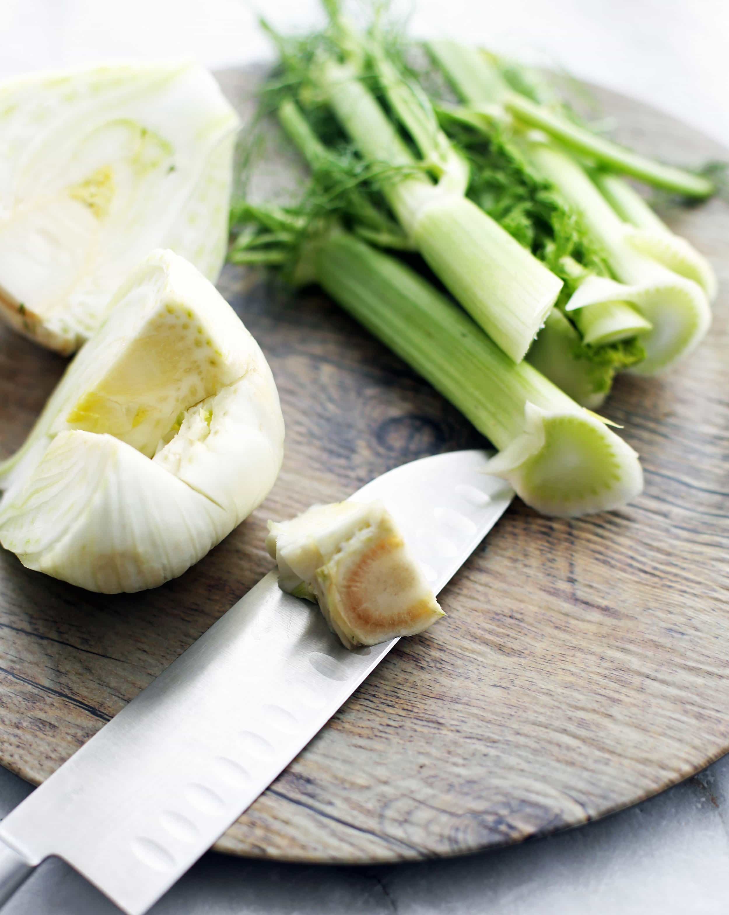 Fennel bulb with tough core cut out of it, that's placed on a sharp knife, all on a wooden platter.