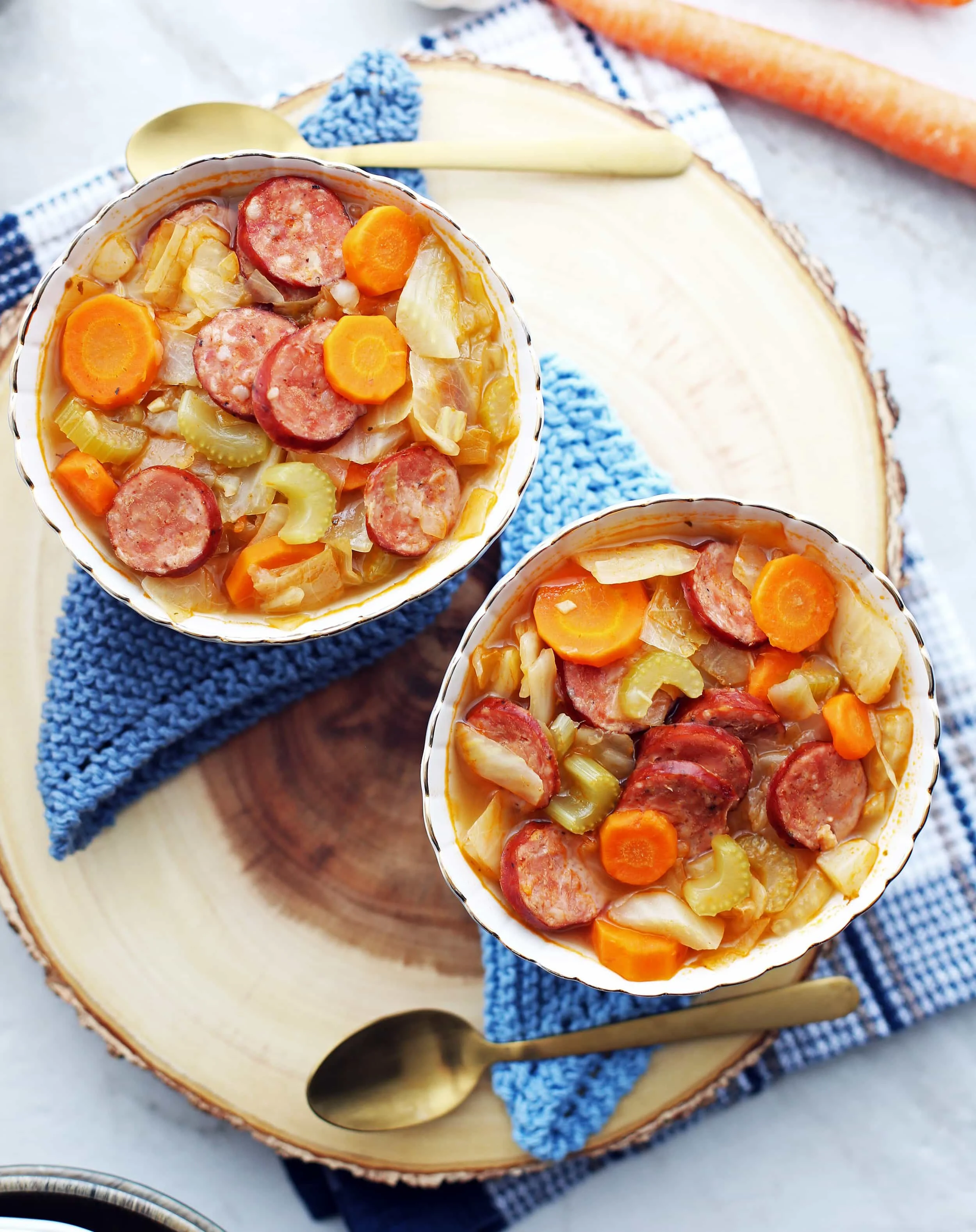 Overhead view of two bowls of fennel, cabbage, and sausage soup on a round wooden board.