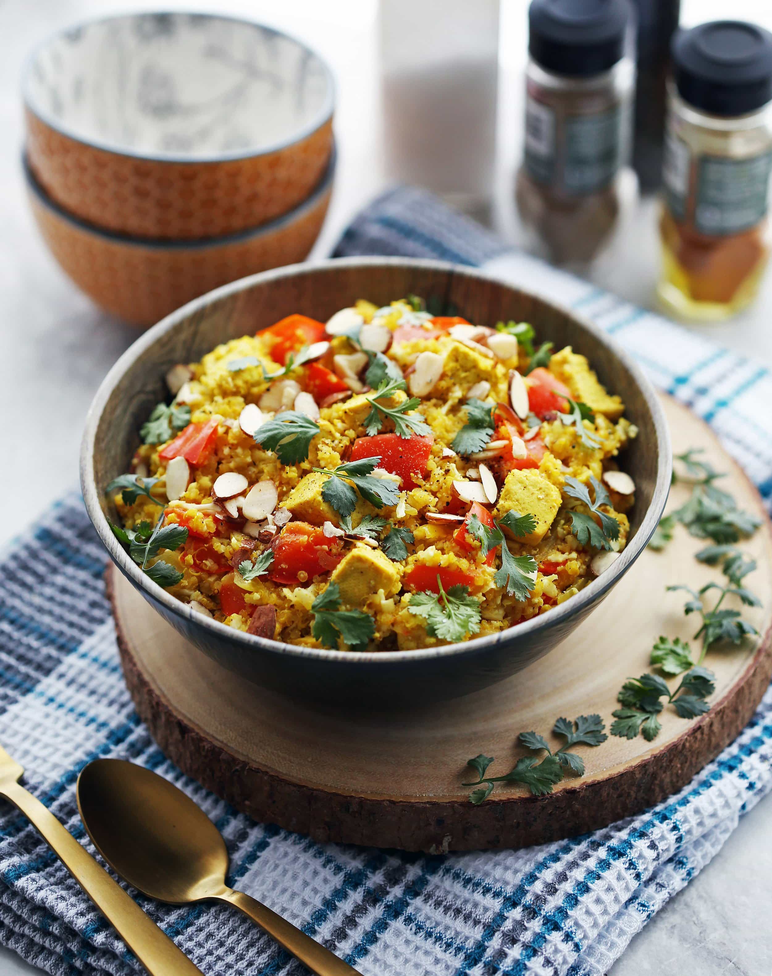 Spiced quinoa, cauliflower rice, tofu, bell pepper, sliced almonds, and cilantro in a large bowl.