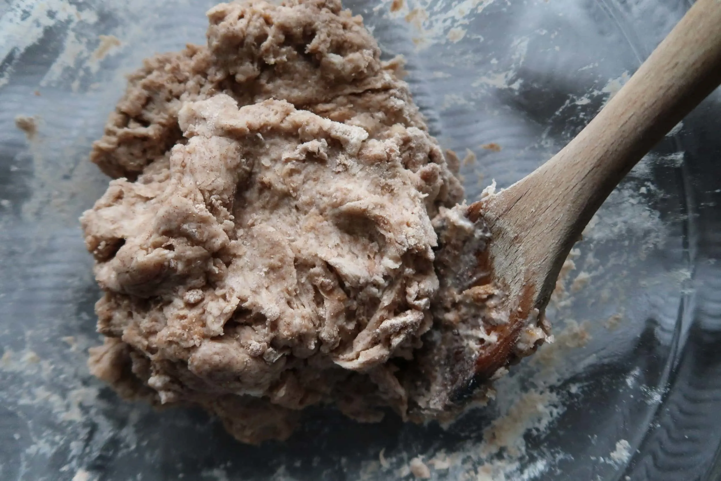 A wooden spoon being used to combine dough ingredients.