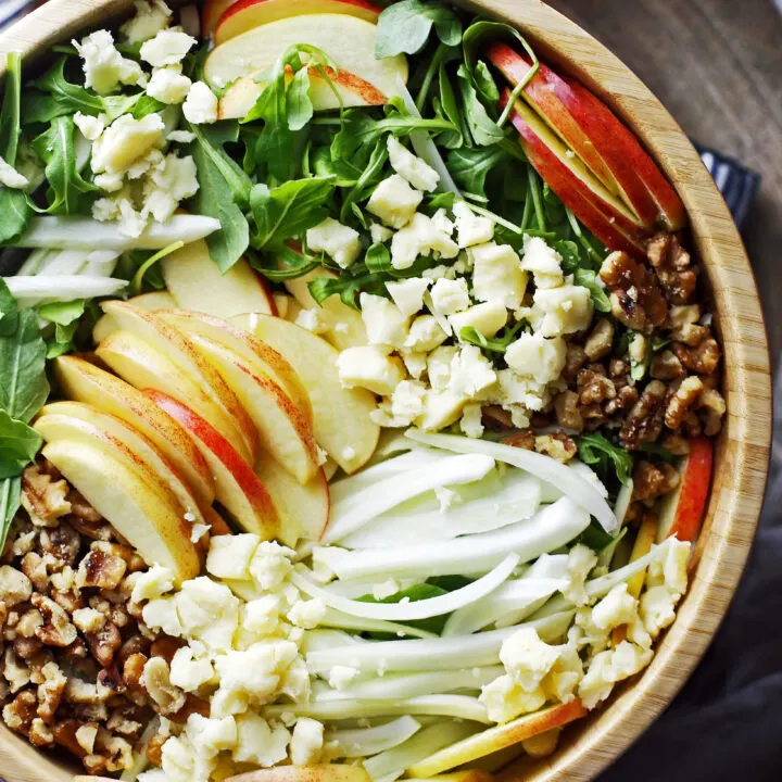 Apple fennel arugula salad with honey lemon vinaigrette in a large wooden bowl.