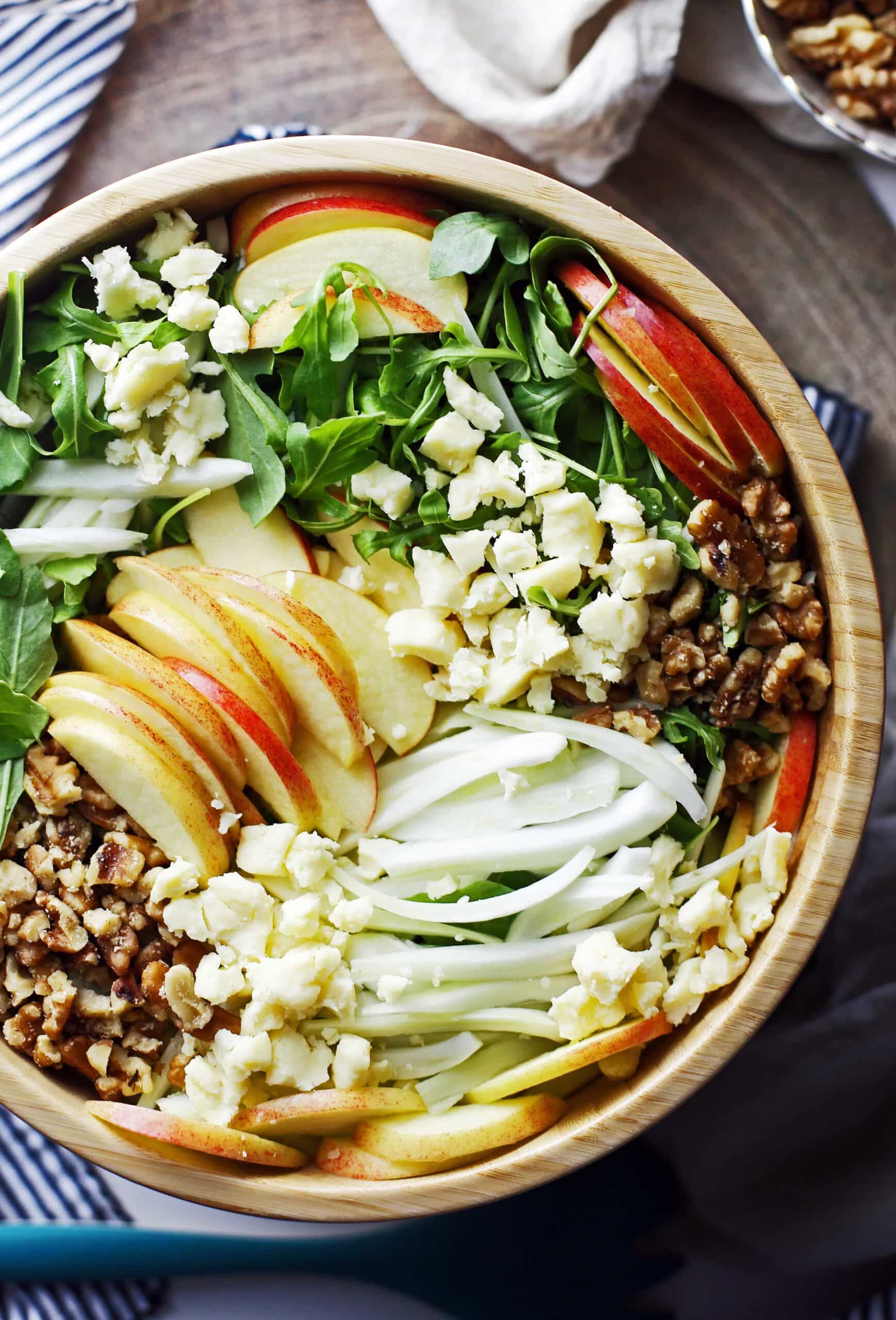 Apple fennel arugula salad with honey lemon vinaigrette in a large wooden bowl.