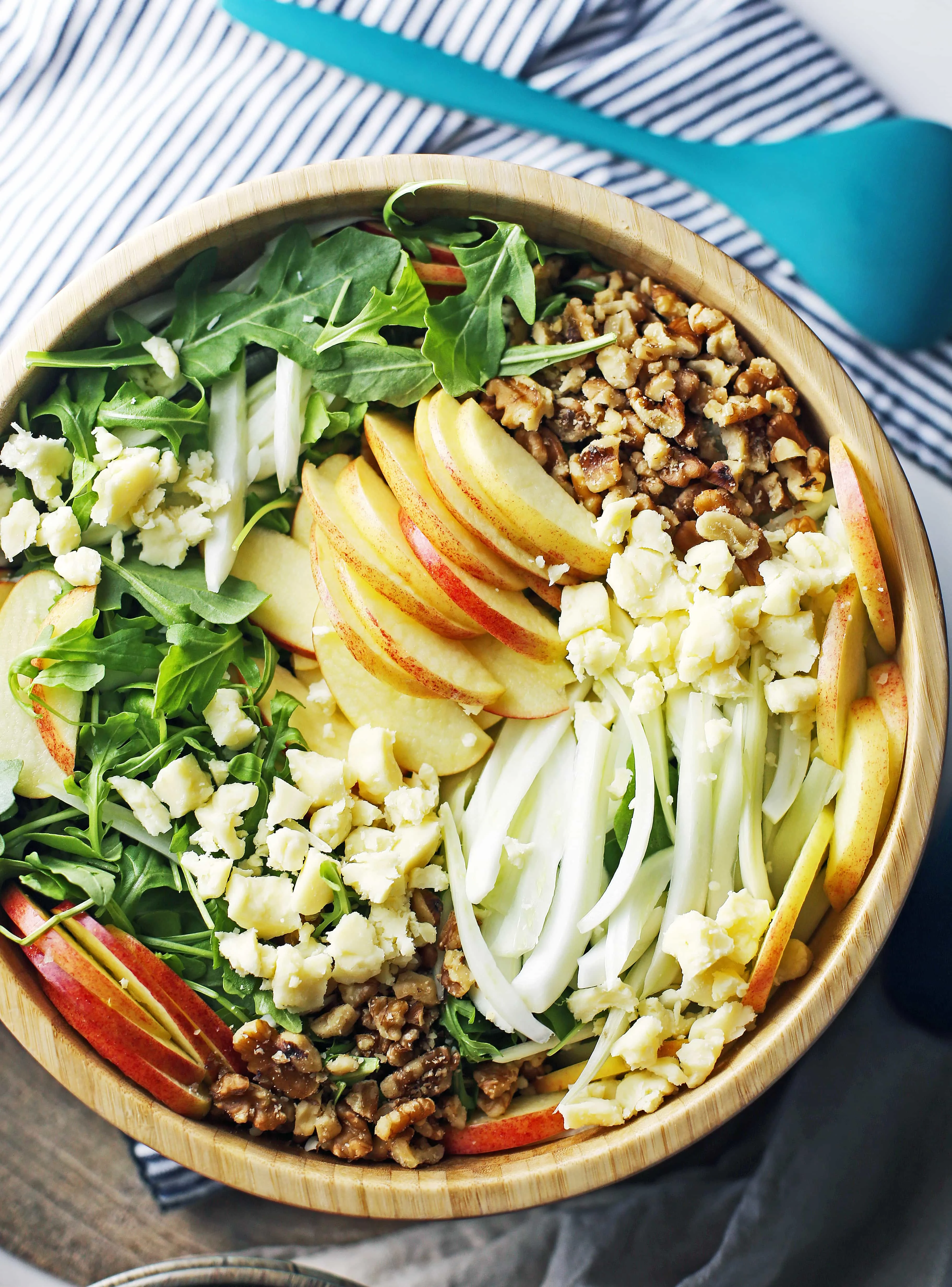 A big wooden bowl containing fennel arugula salad with apples and walnuts.
