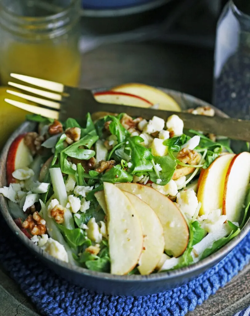 Apple fennel arugula salad in a brown bowl with a fork on top.