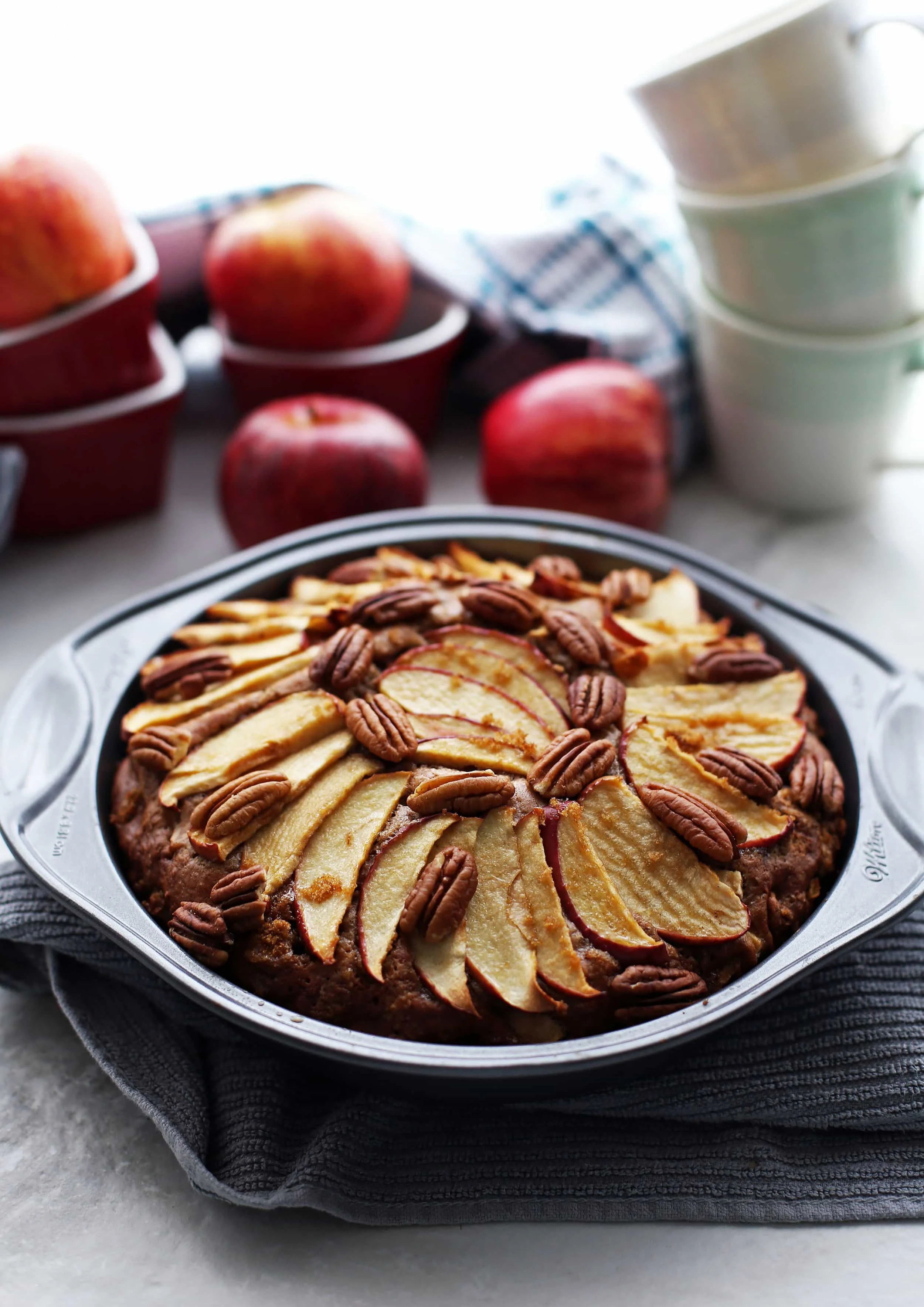 Baked apple cinnamon pecan cake with apple slices and pecans on top in a round cake pan.