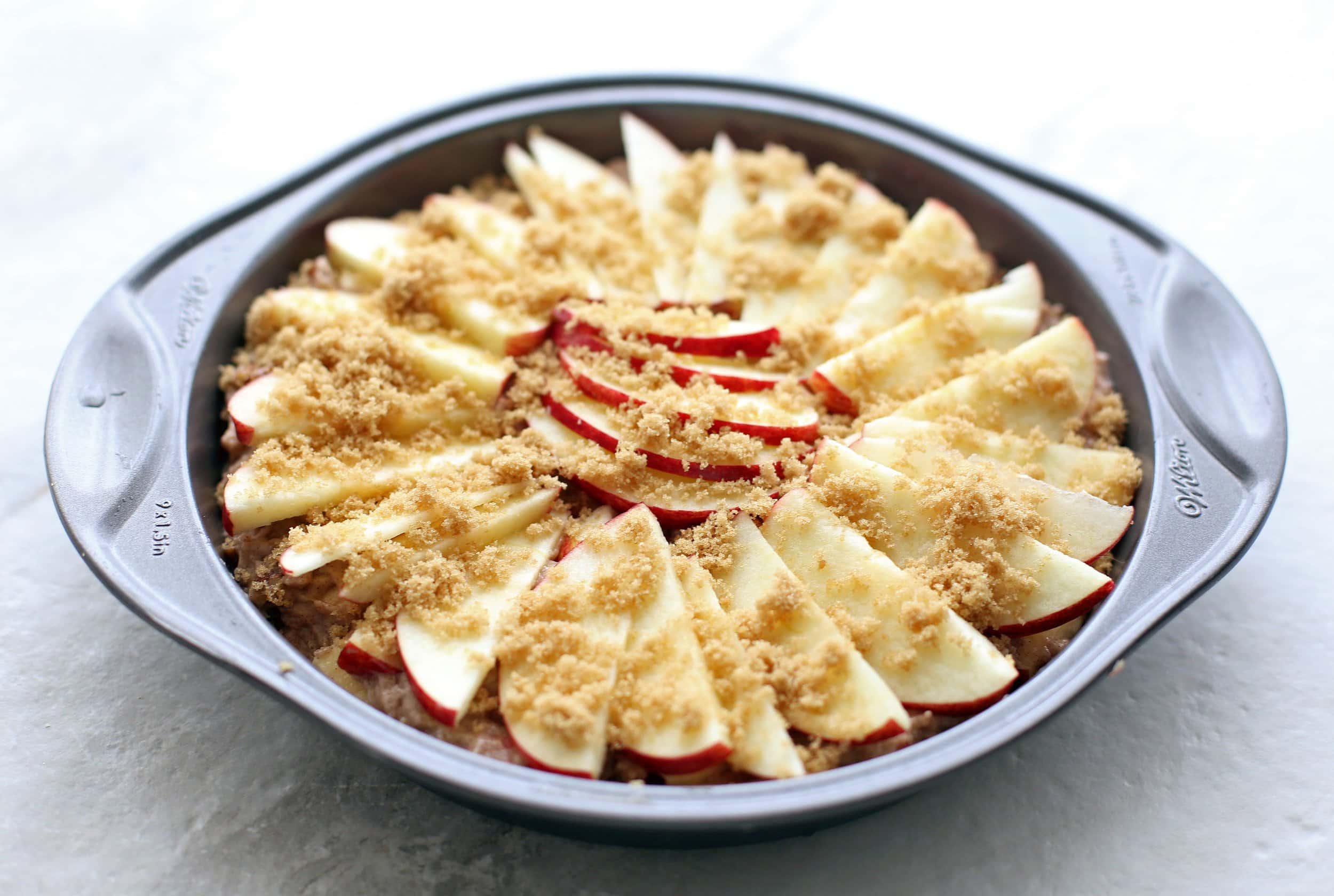 Apple cinnamon pecan cake batter with apple slice pattern on top in a round cake pan.