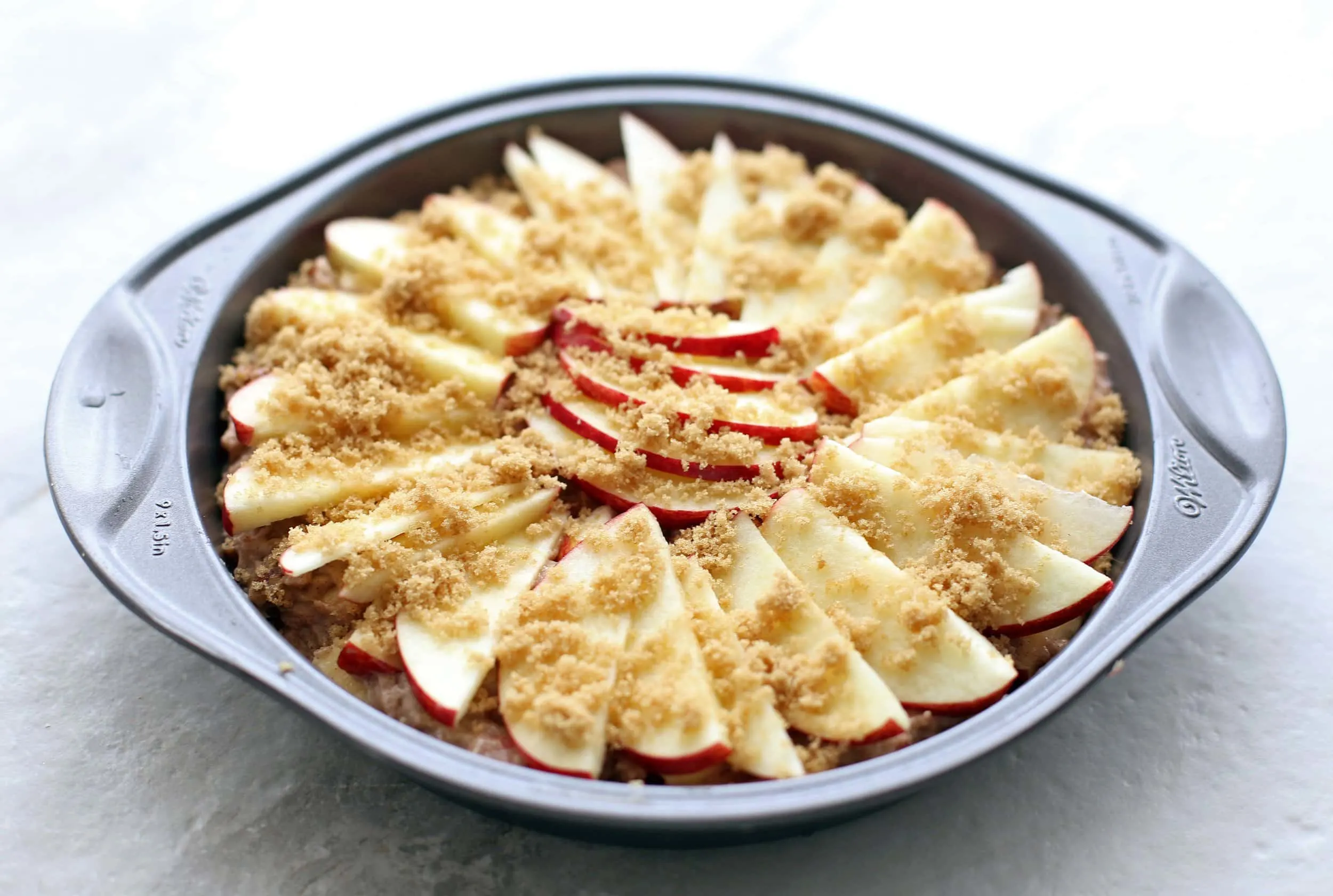 Apple cinnamon pecan cake batter with apple slice pattern on top in a round cake pan.