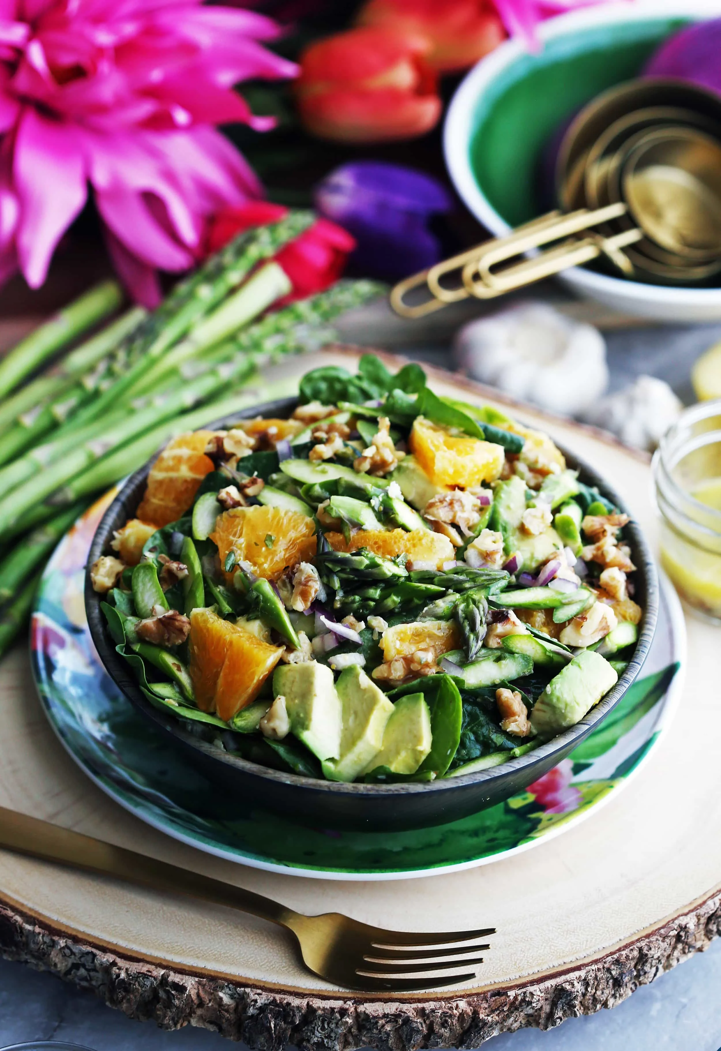 A wooden bowl full of Asparagus Orange Spinach Salad with Basil Lemon Vinaigrette along with a fork beside it.