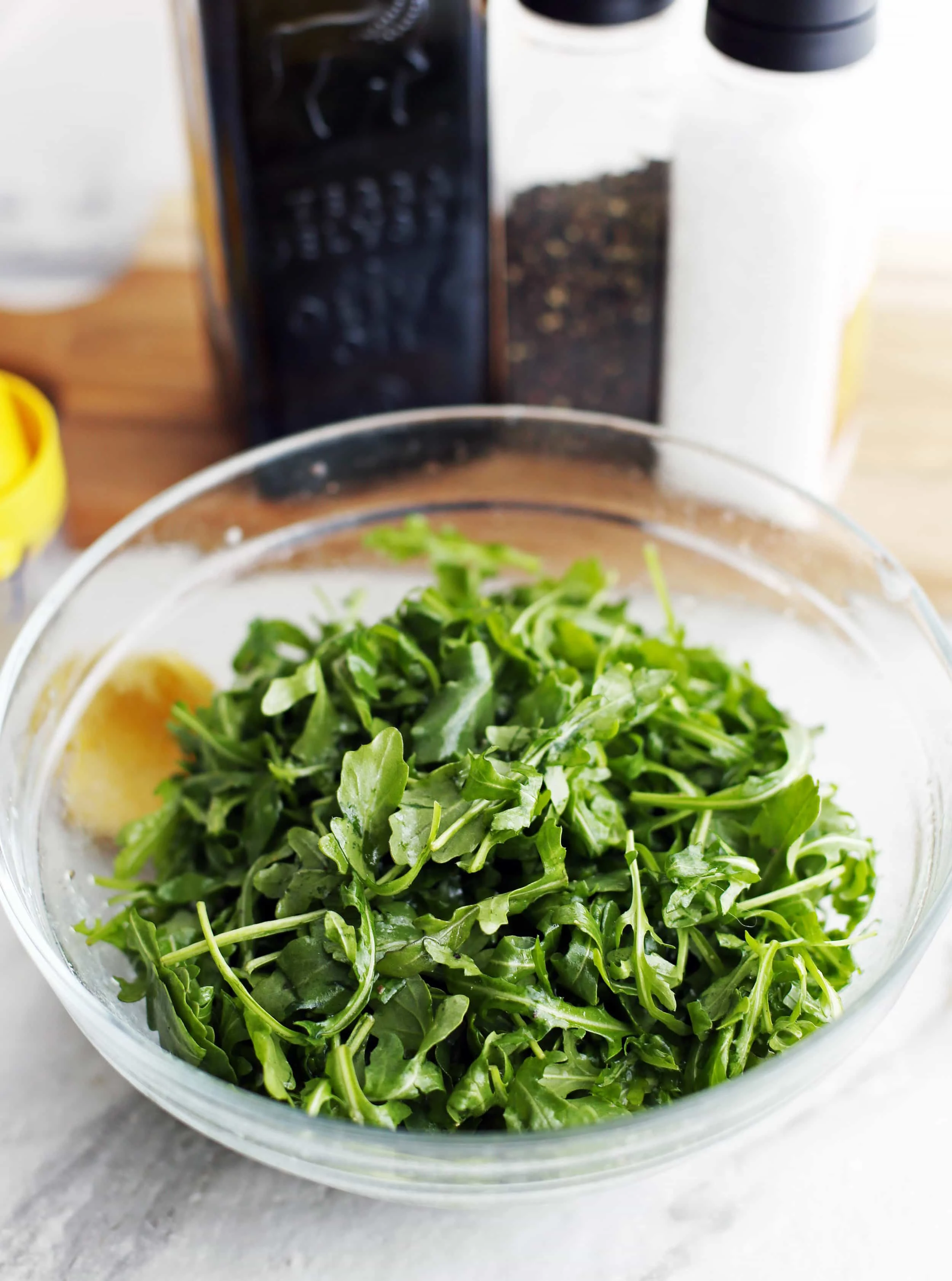 Baby arugula that has been tossed with olive oil, lemon juice, salt, and pepper in a glass bowl.