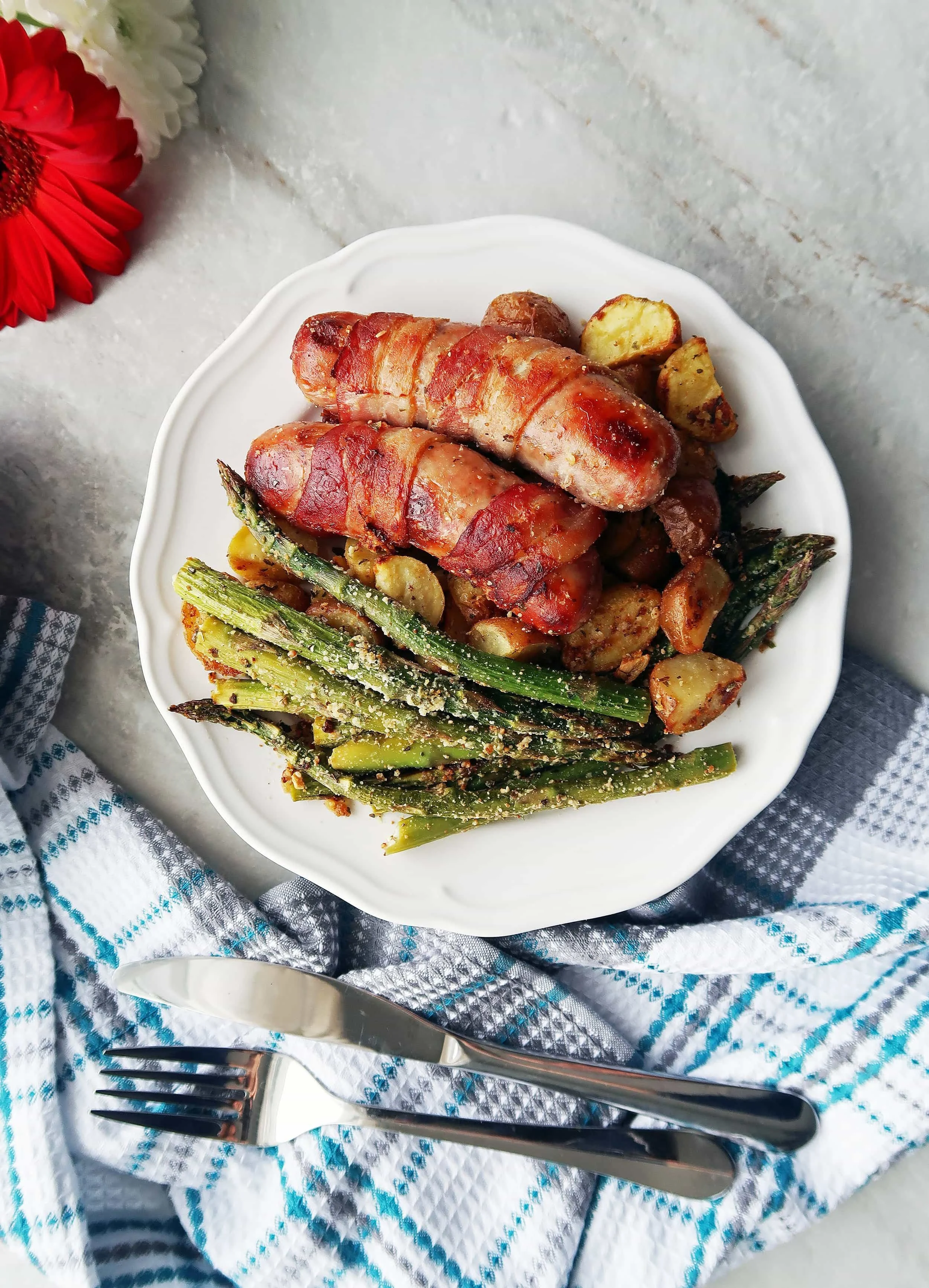 A plate of Bacon-Wrapped Sausages with Garlic Parmesan Asparagus and Potatoes