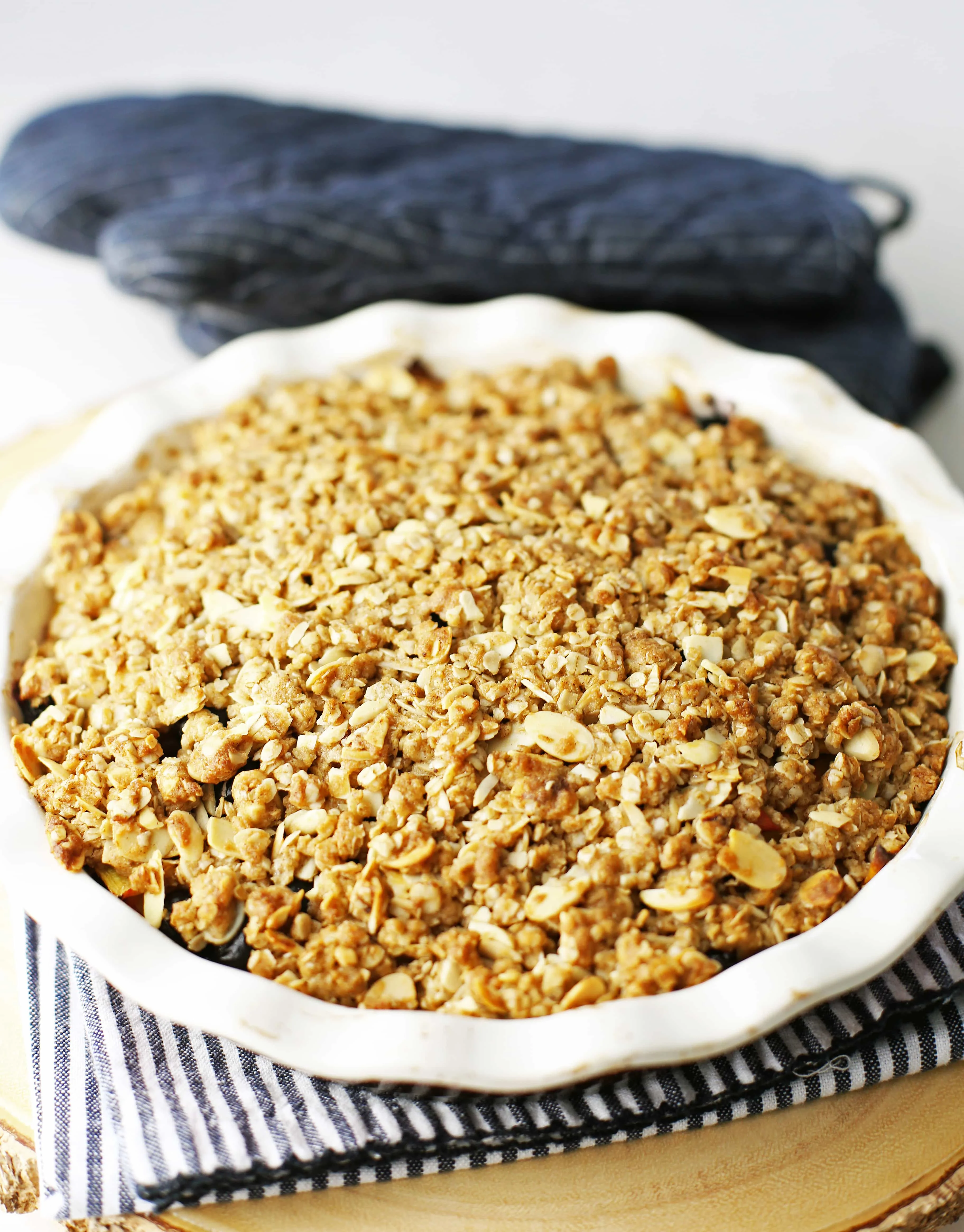 Baked blueberry peach crisp with almond oat topping in a pie dish on top of a white and blue towel.