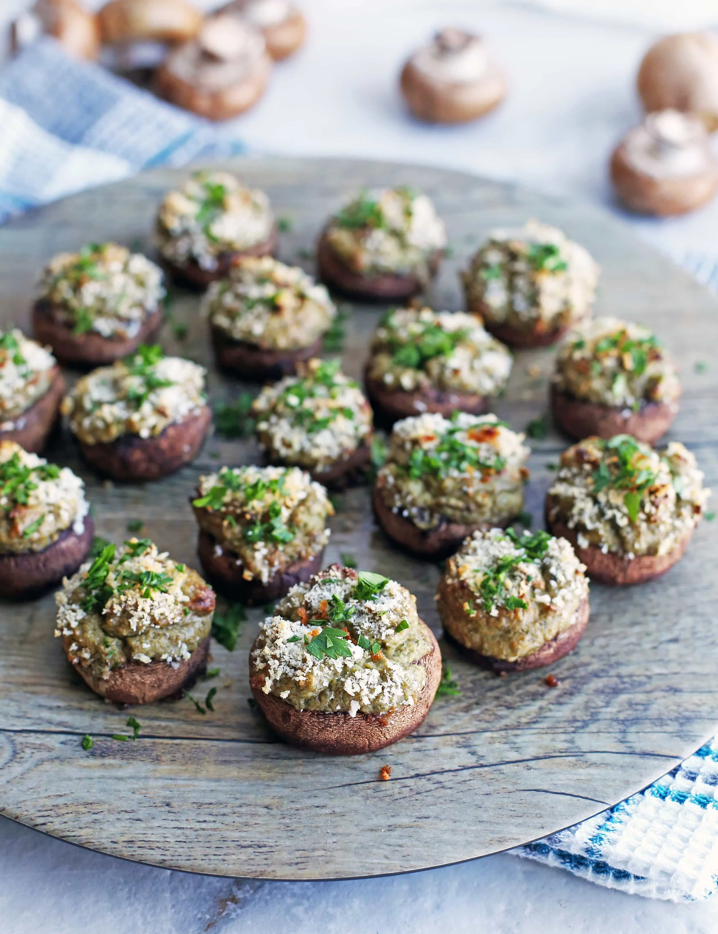 Over a dozen Baked Cheese Stuffed Mushrooms topped with breadcrumbs and chopped parsley on a round platter.