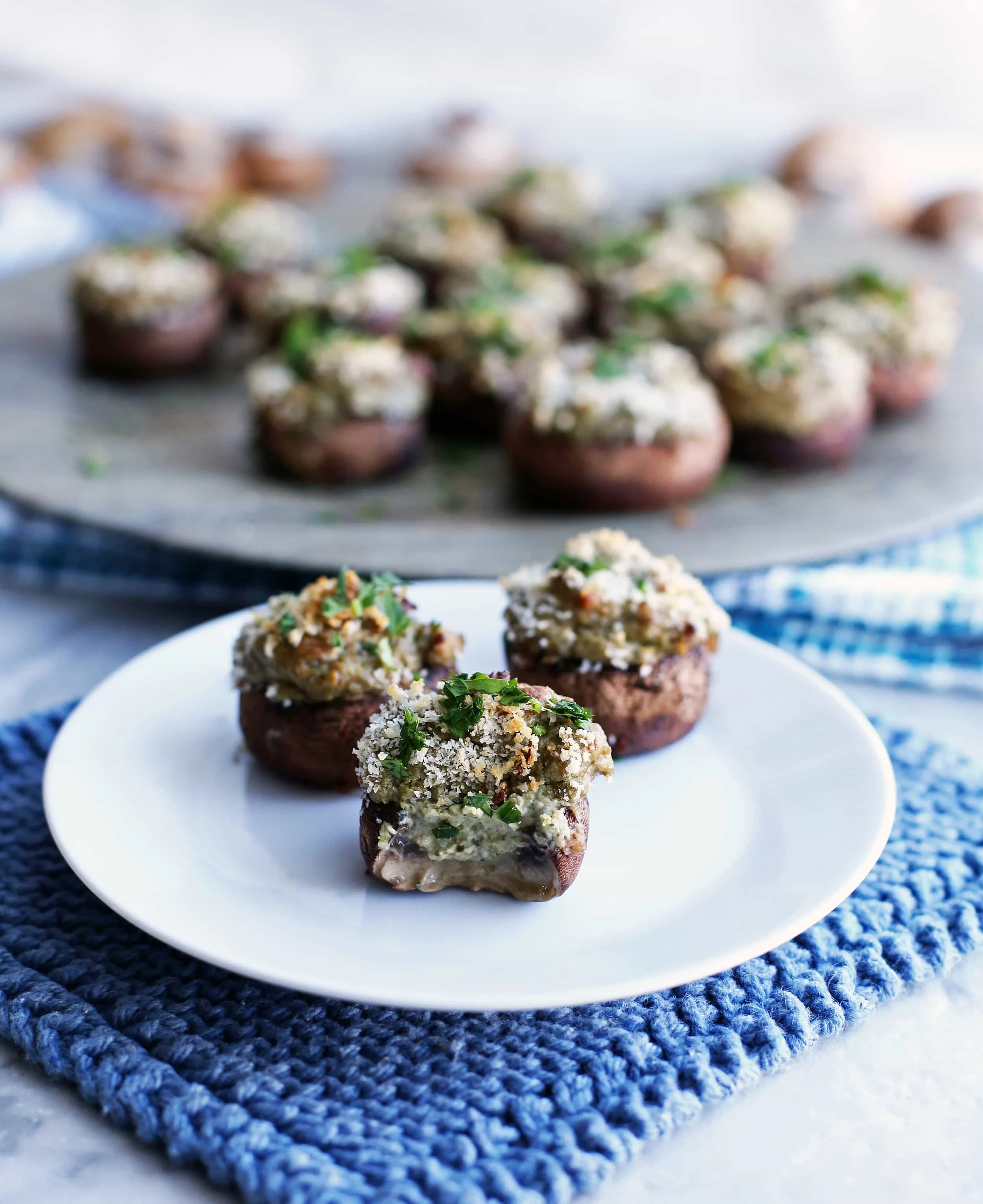 Three baked cheese stuffed mushrooms on a white plate with a bite taken out of one.