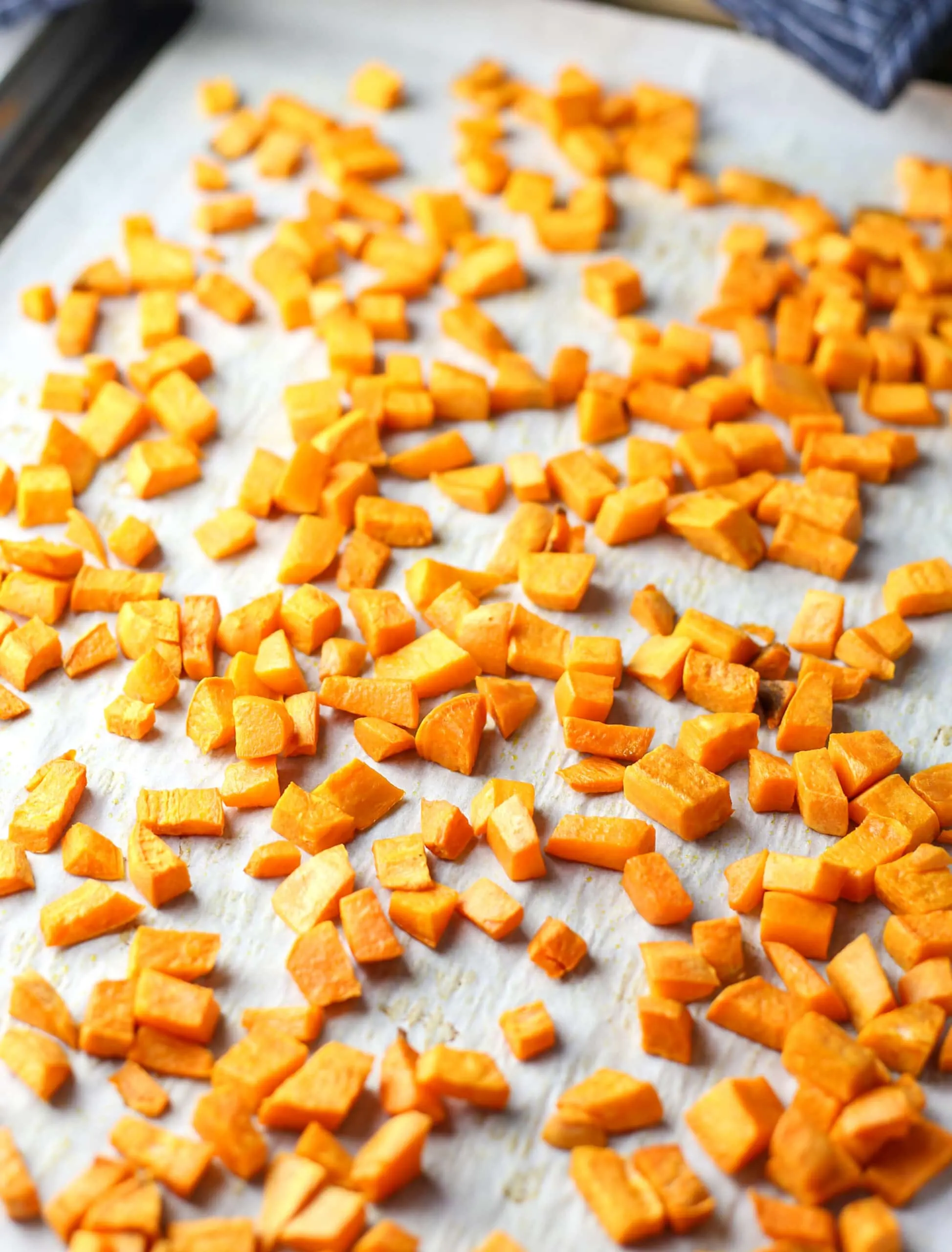 Chopped roasted butternut squash on a parchment paper lined baking sheet.