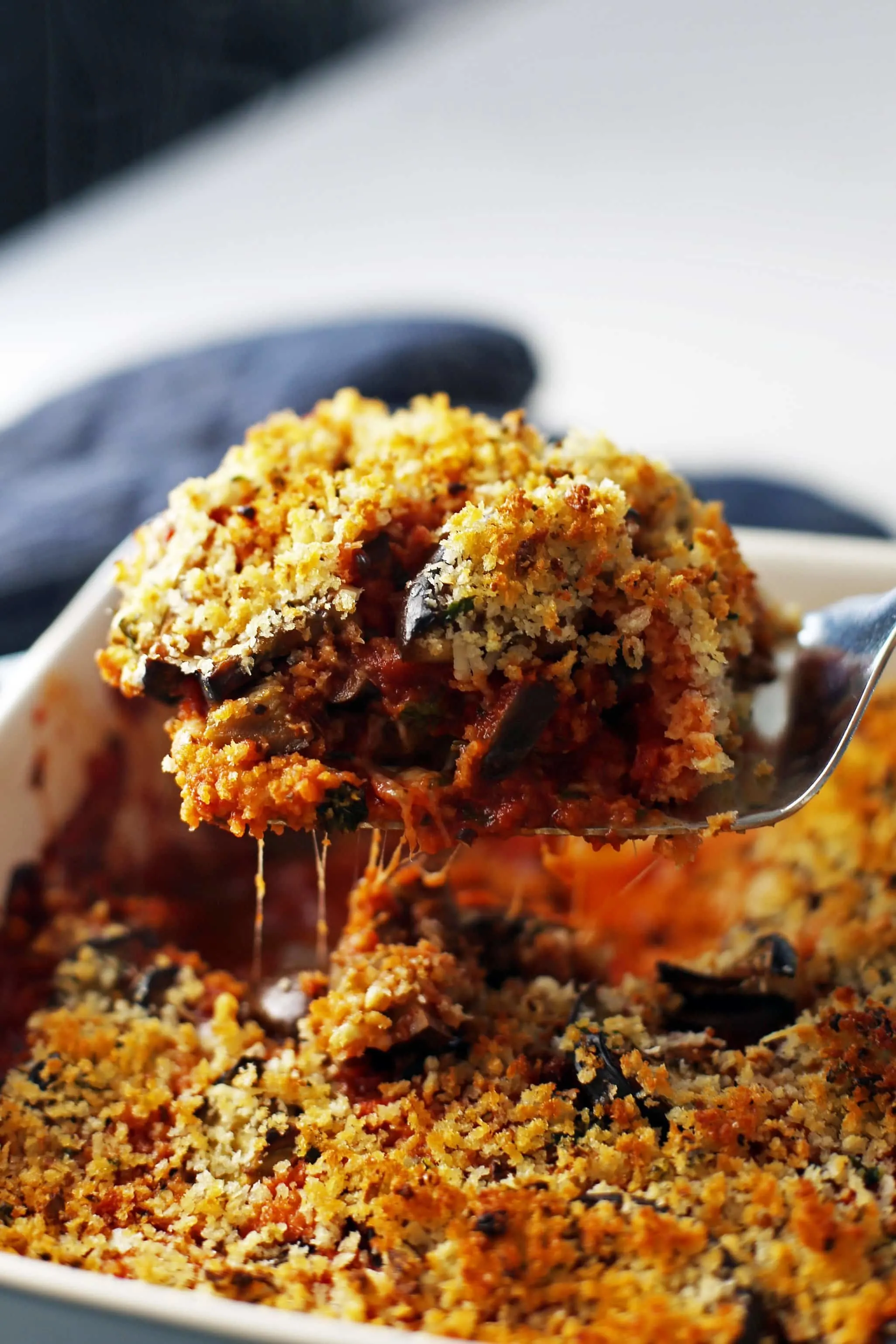 A generous piece of cheesy baked eggplant parmesan being scooped out a large casserole dish.