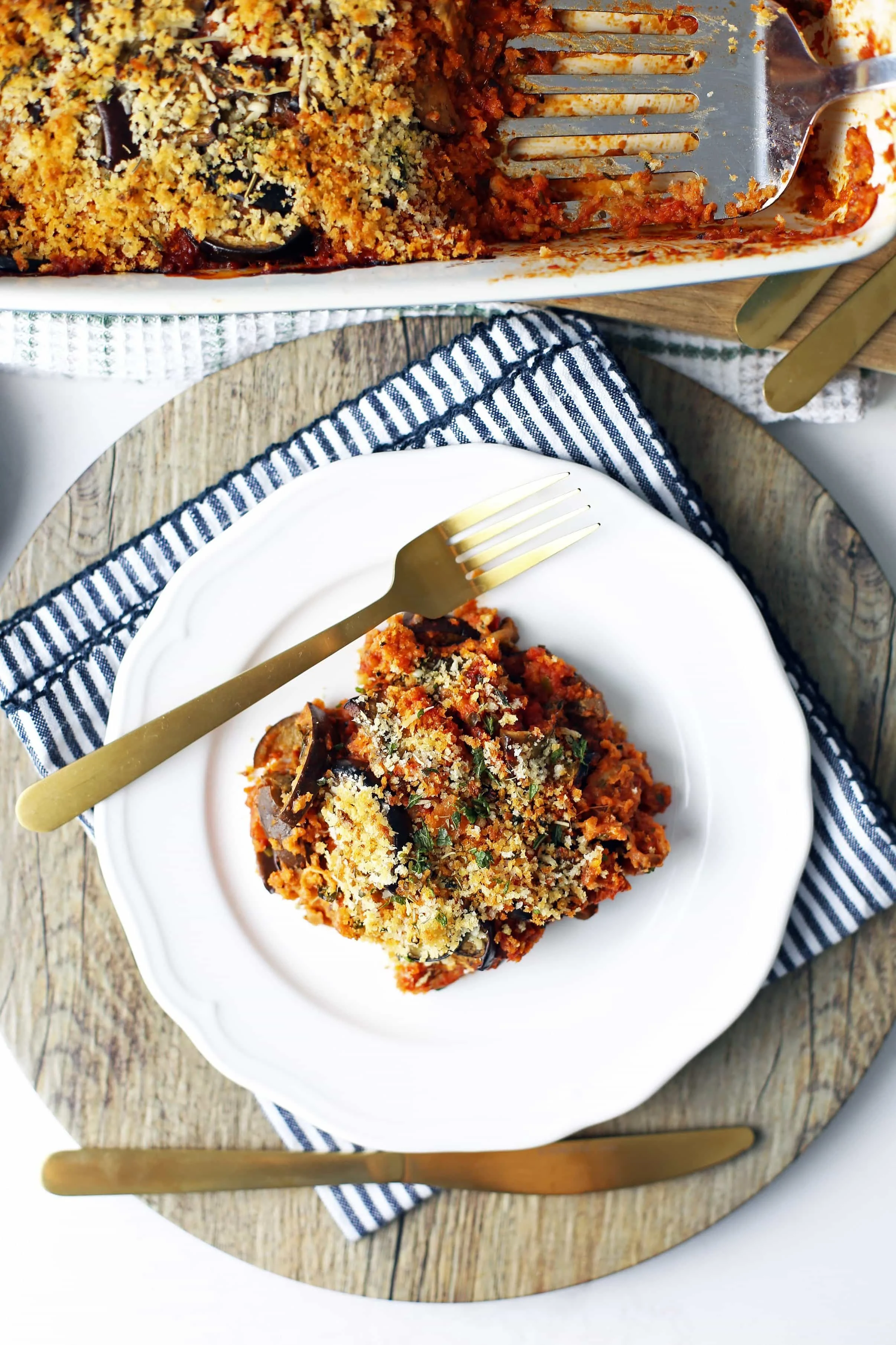 Overhead view of Baked Eggplant Parmesan on a white plate and large rectangular dish.