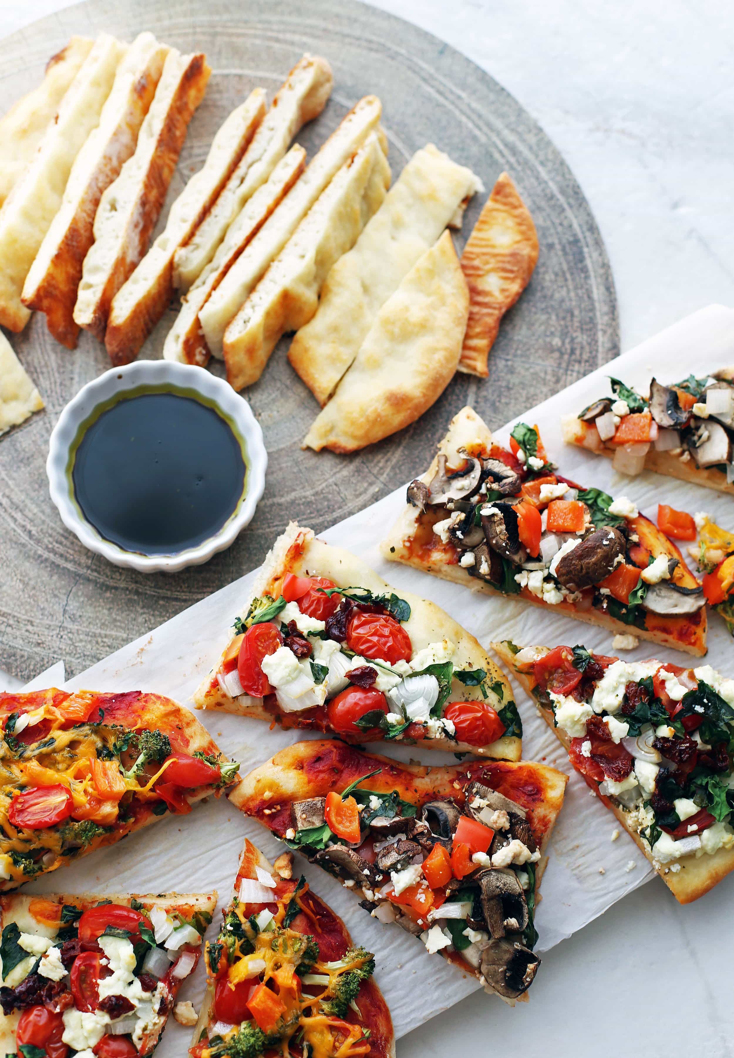 Overhead view of flatbread pizza slices and sliced four-ingredient flatbread with dip on two platters.