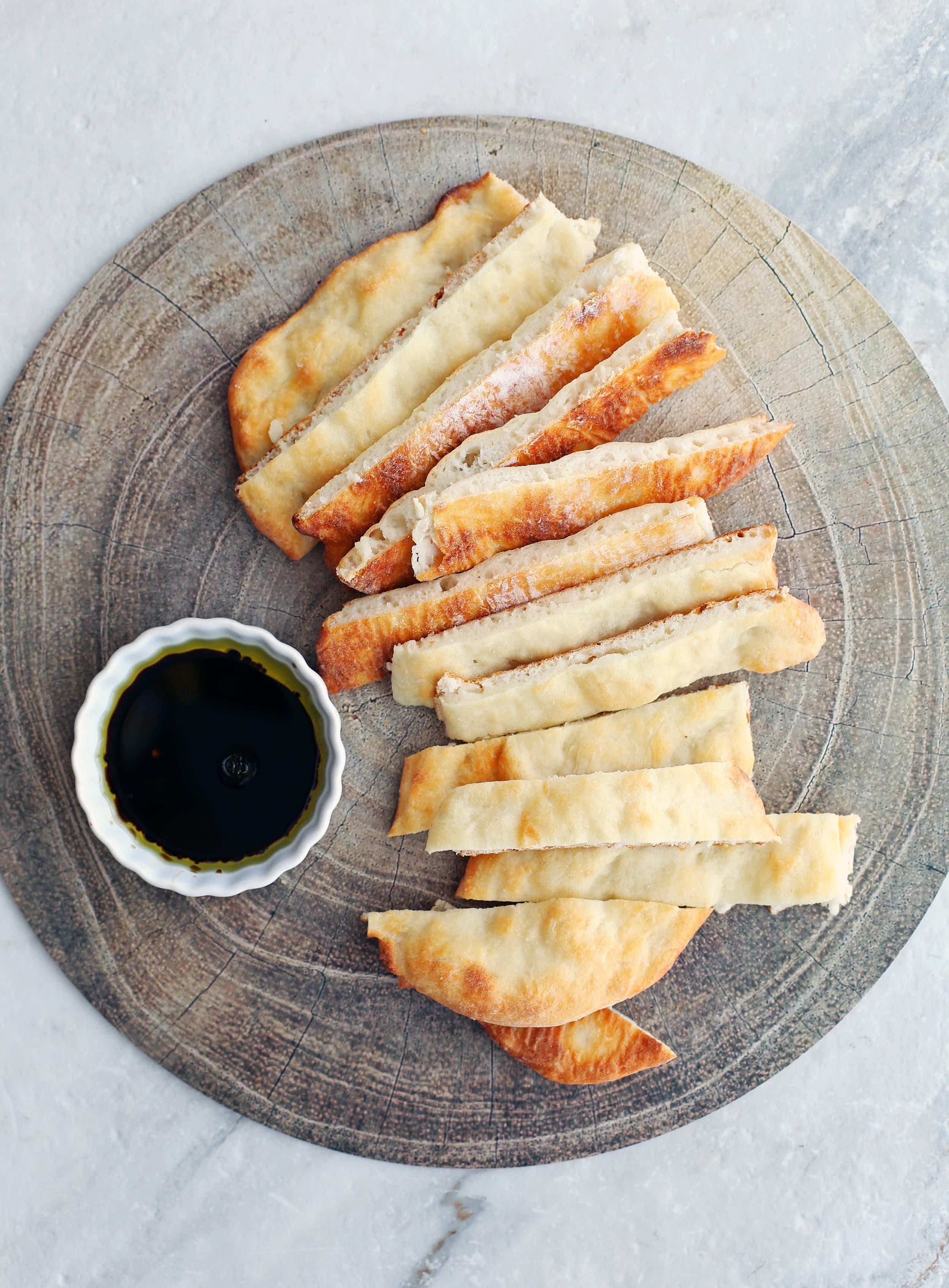 Sliced four-ingredient baked flatbread with balsamic-olive oil dip on a round platter.