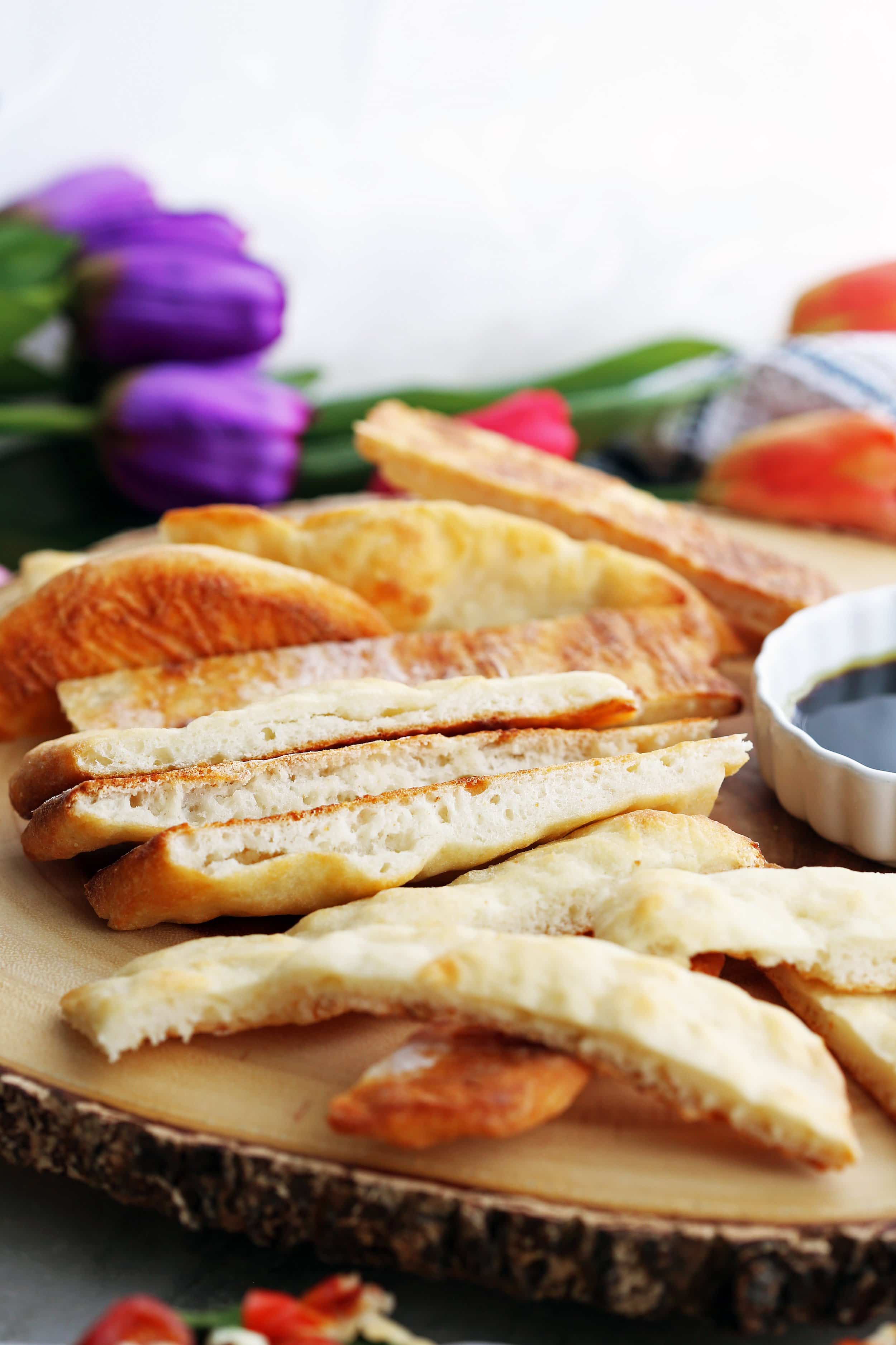 Close-up of sliced four-ingredient baked flatbread on round wooden platter.