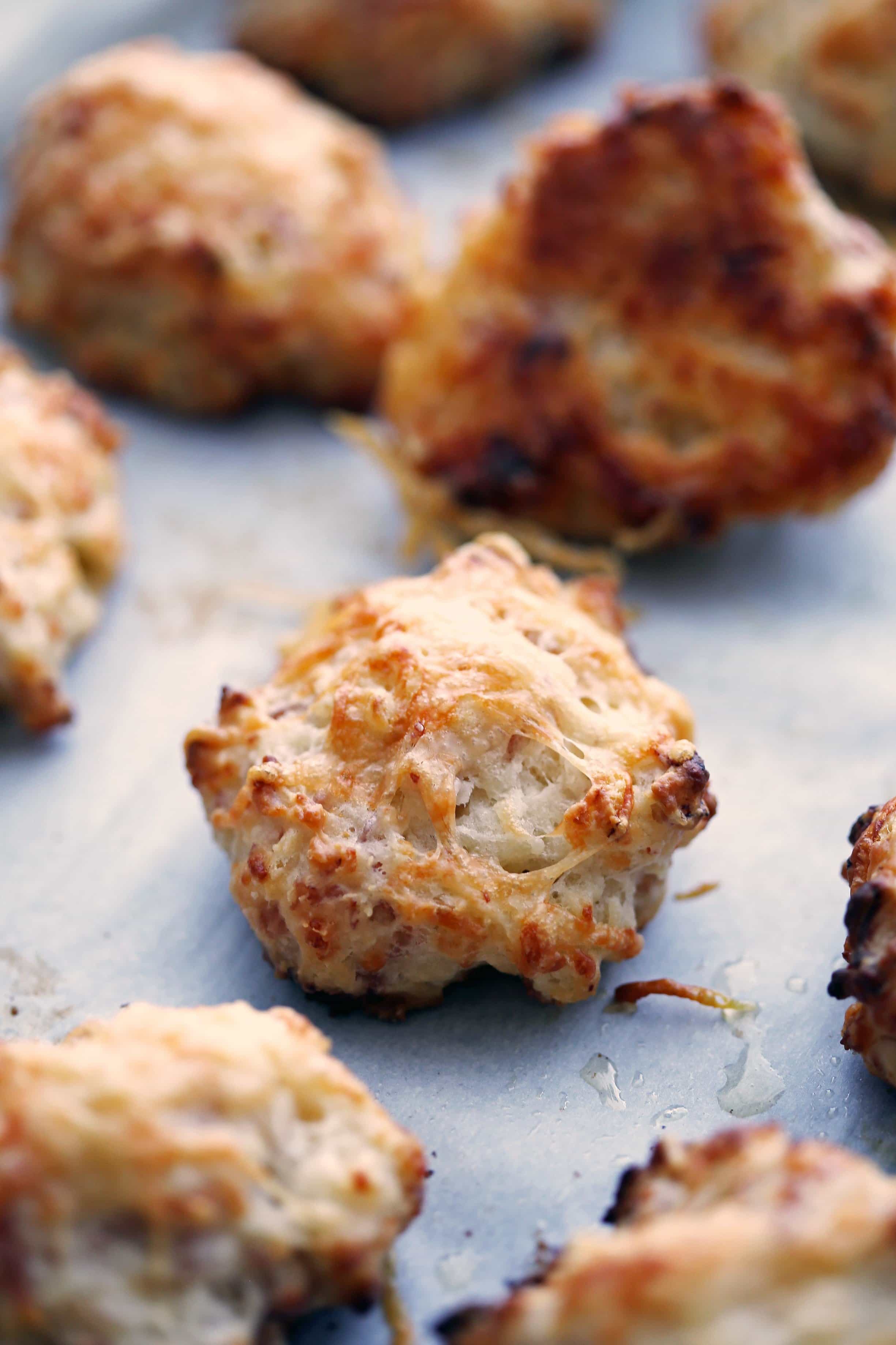 A closeup of a freshly baked ham and cheese drop biscuit surrounded by more drop biscuits on parchment paper.