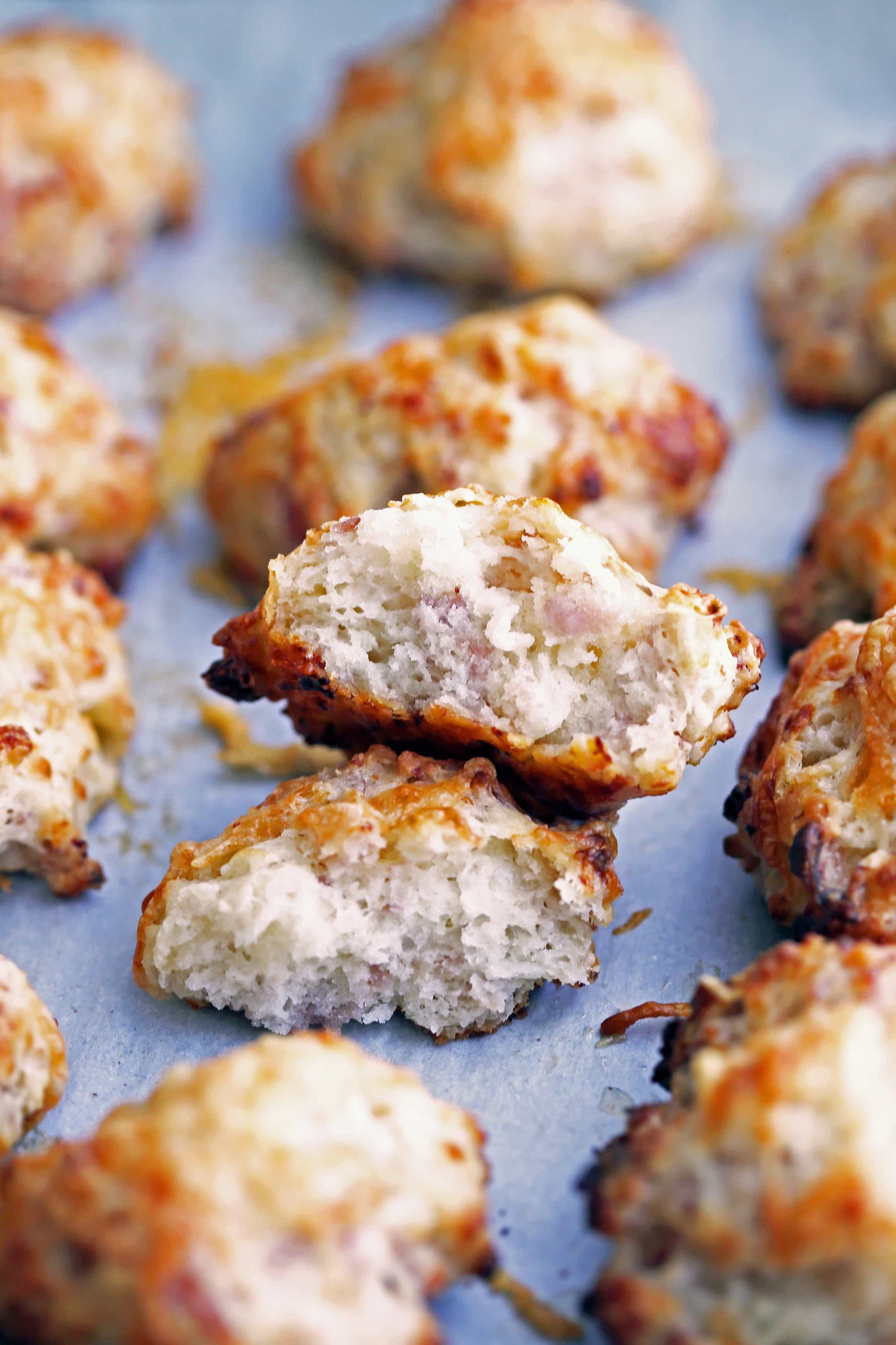 A ham and cheese drop biscuit broken in half that’s surrounded by more drop biscuits on parchment paper.