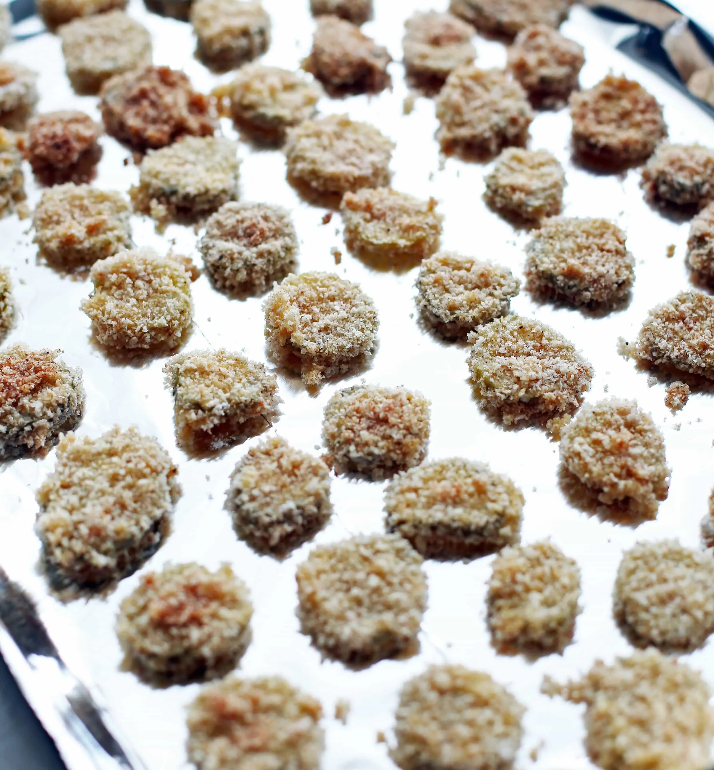 Dredged panko breadcrumb covered pickle slices placed on an aluminum foil lined baking sheet.