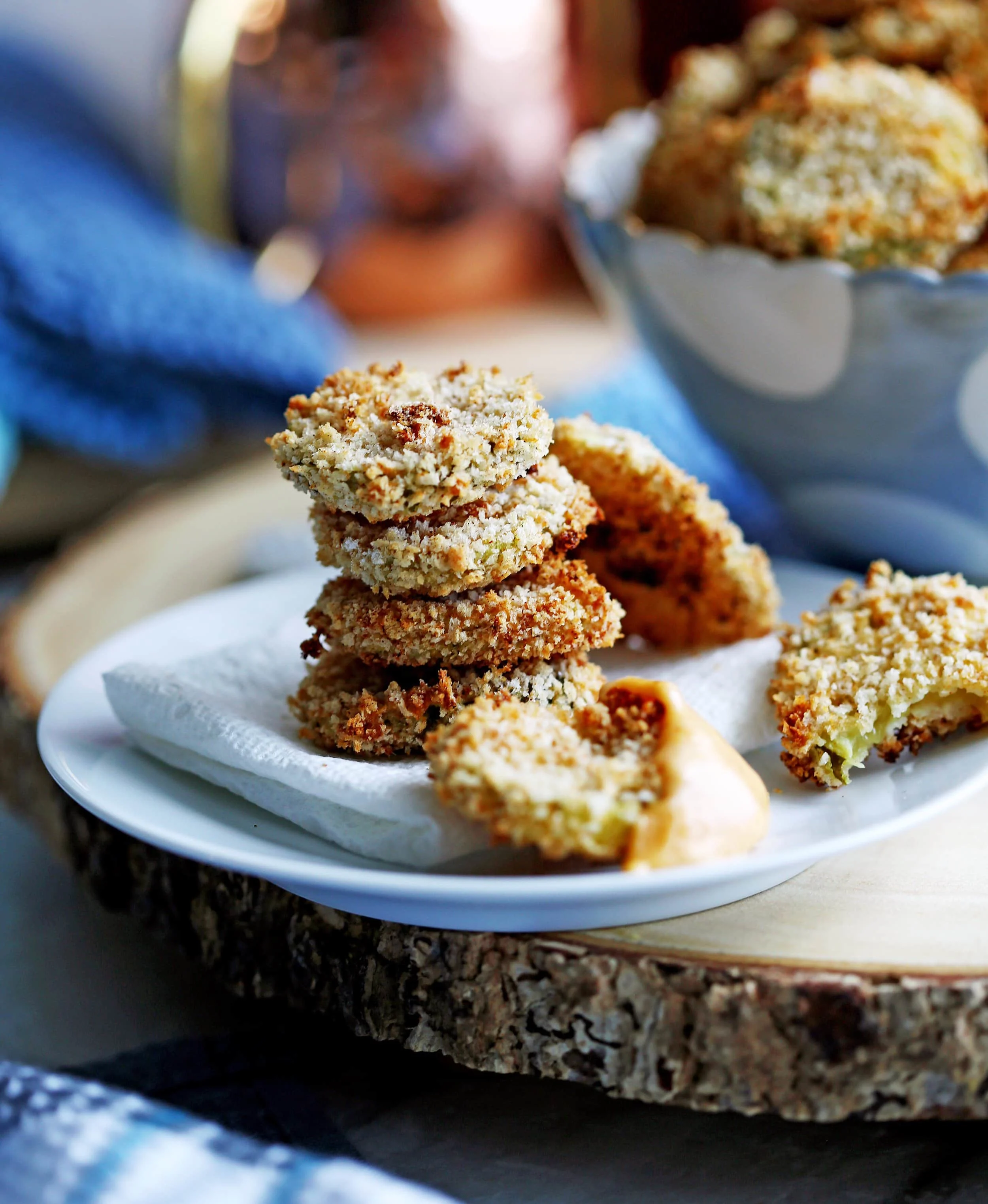 A side view of four stacked crispy oven-fried pickles. To the side, one oven-fried pickle is covered with cheddar sauce.