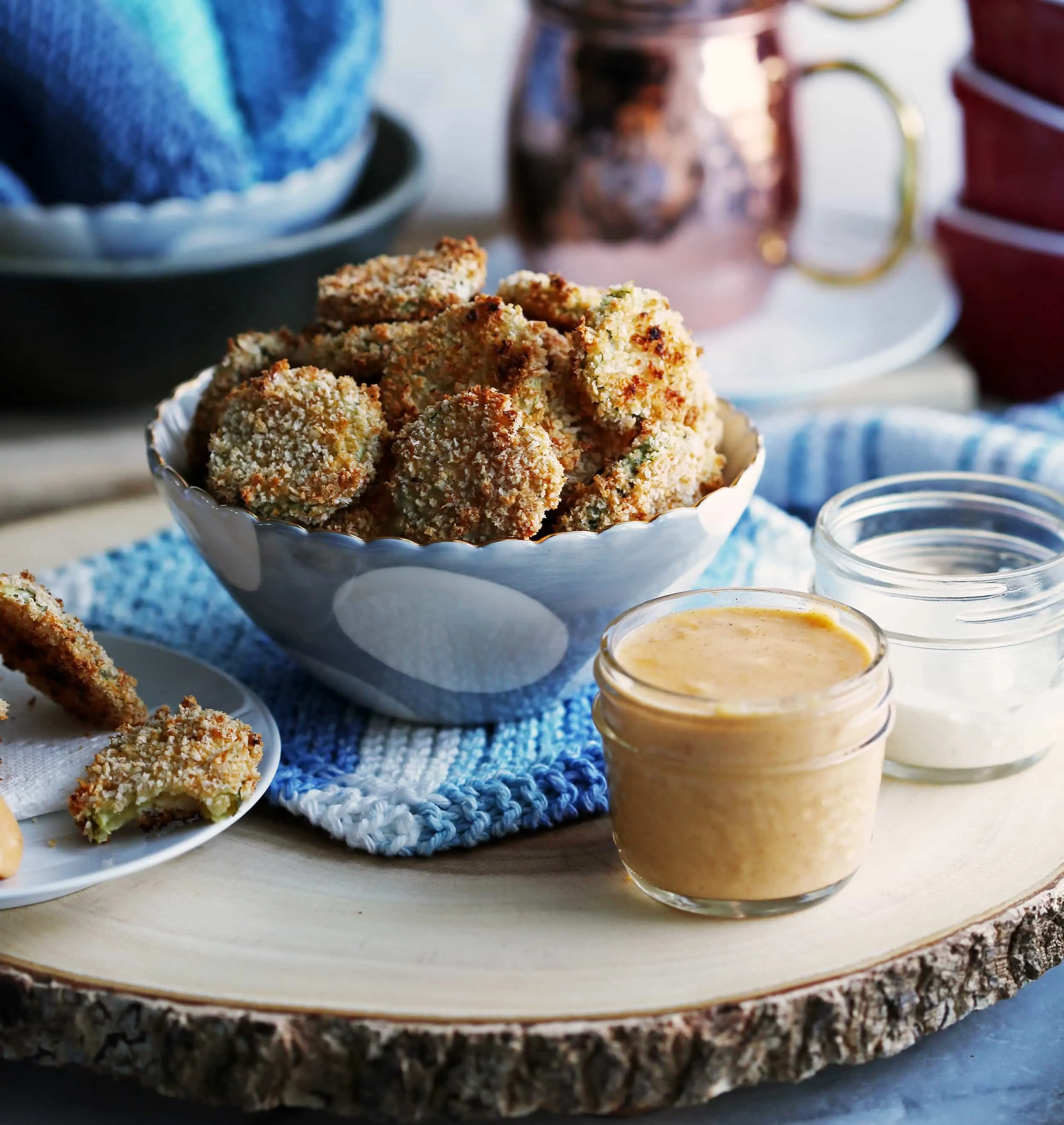 A blue bowl of crispy oven-fried pickles slices with a jar of creamy cheddar dip on the side.