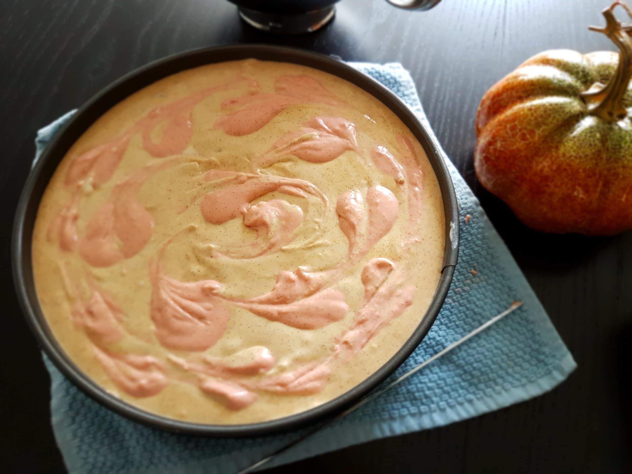 Cheesecake batter in a springform pan with faint, red swirls on top.