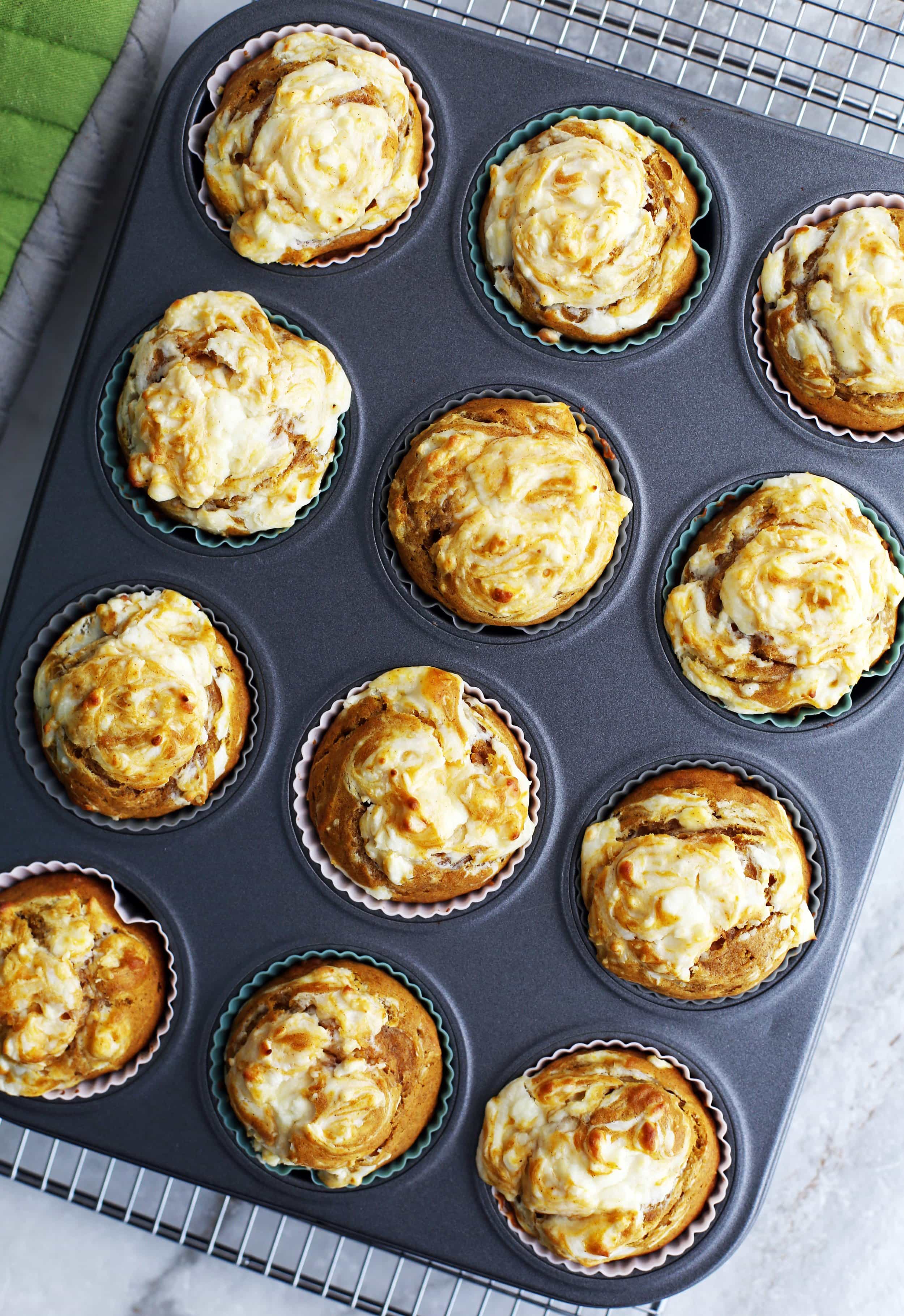 Twelve baked pumpkin cream cheese muffins in a muffin pan.