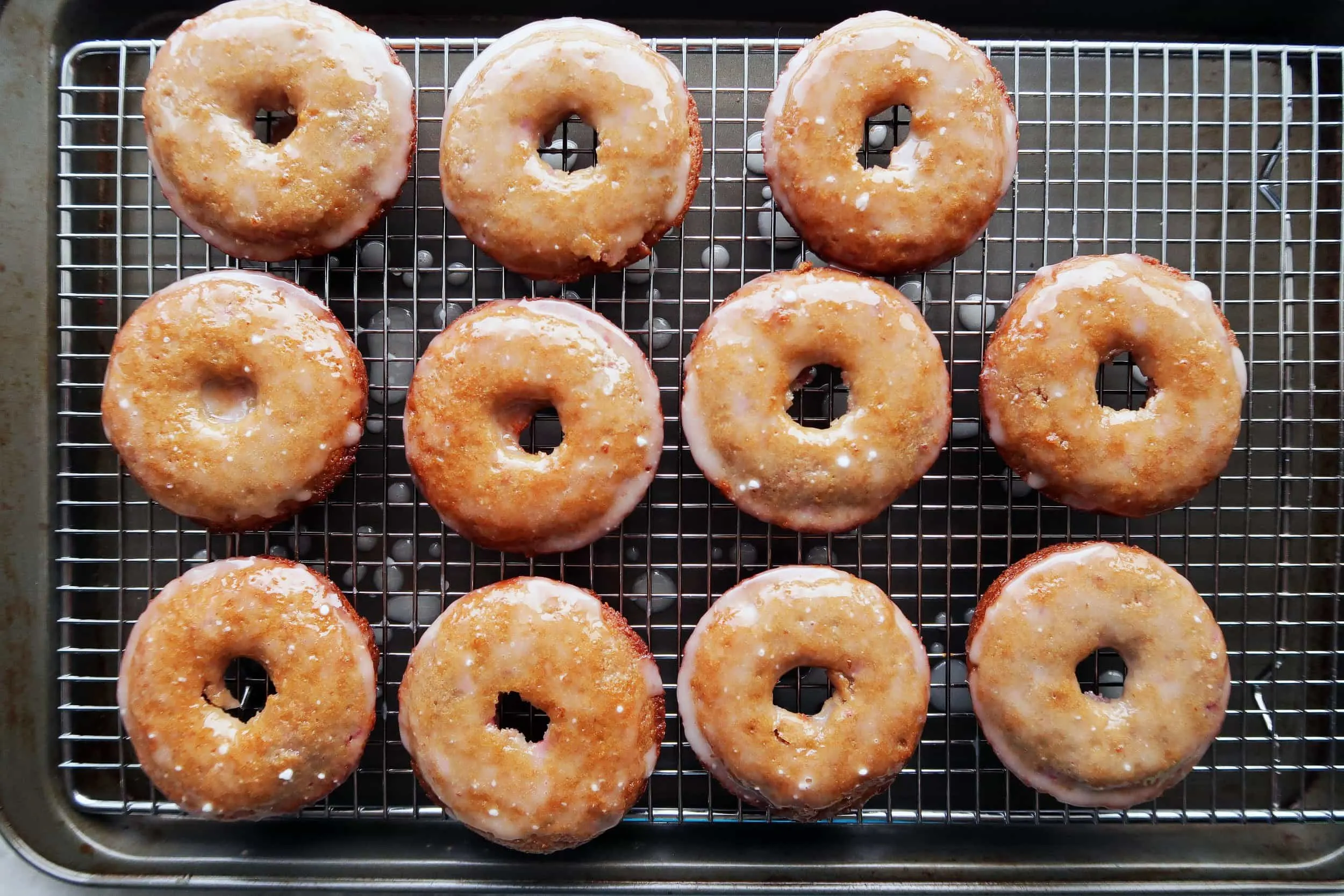 Ten Baked Raspberry Lemon Donuts that are freshly glazed on a cooling rack.