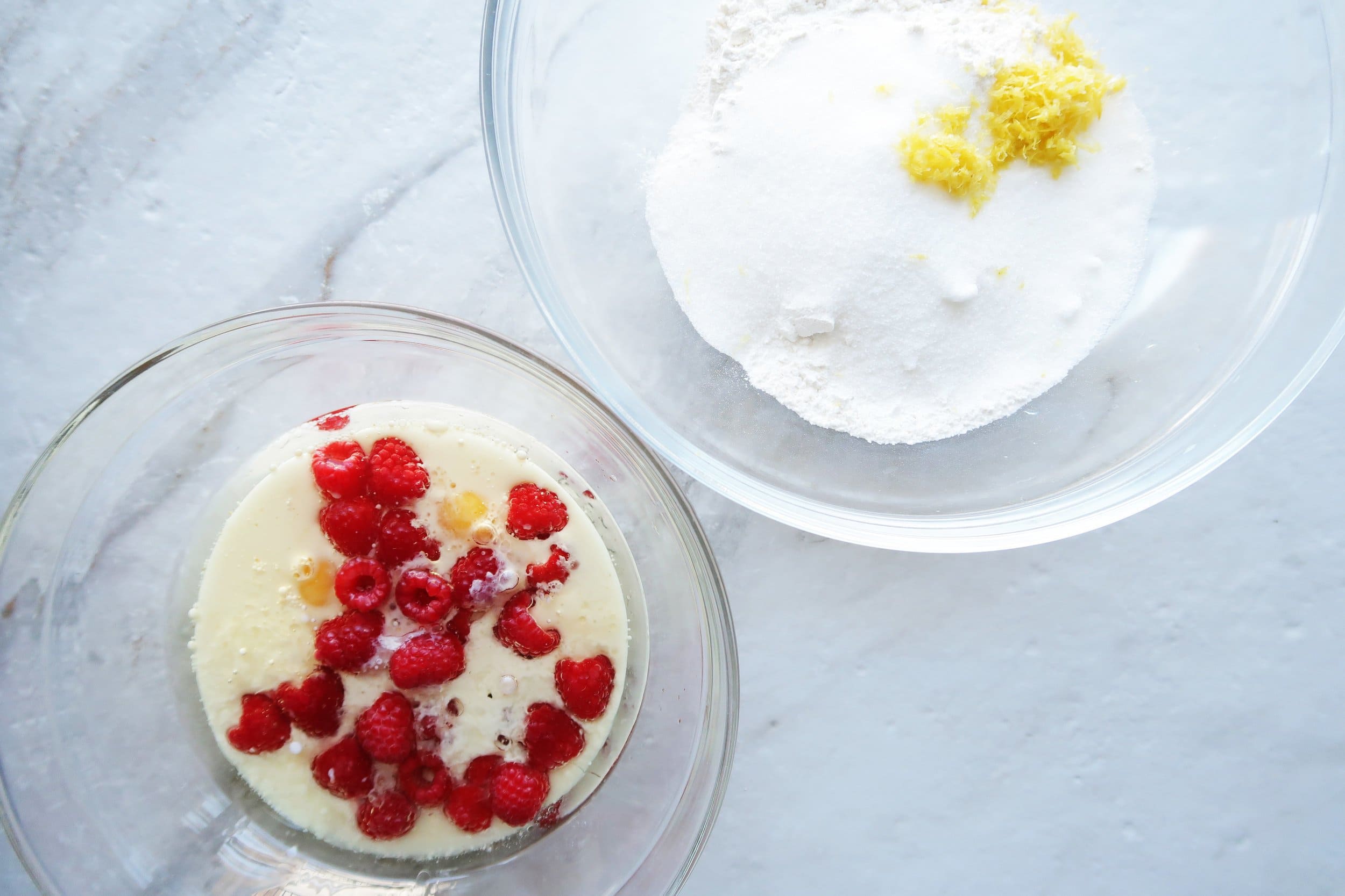 Bowls of dry and wet ingredients featuring whole raspberries.