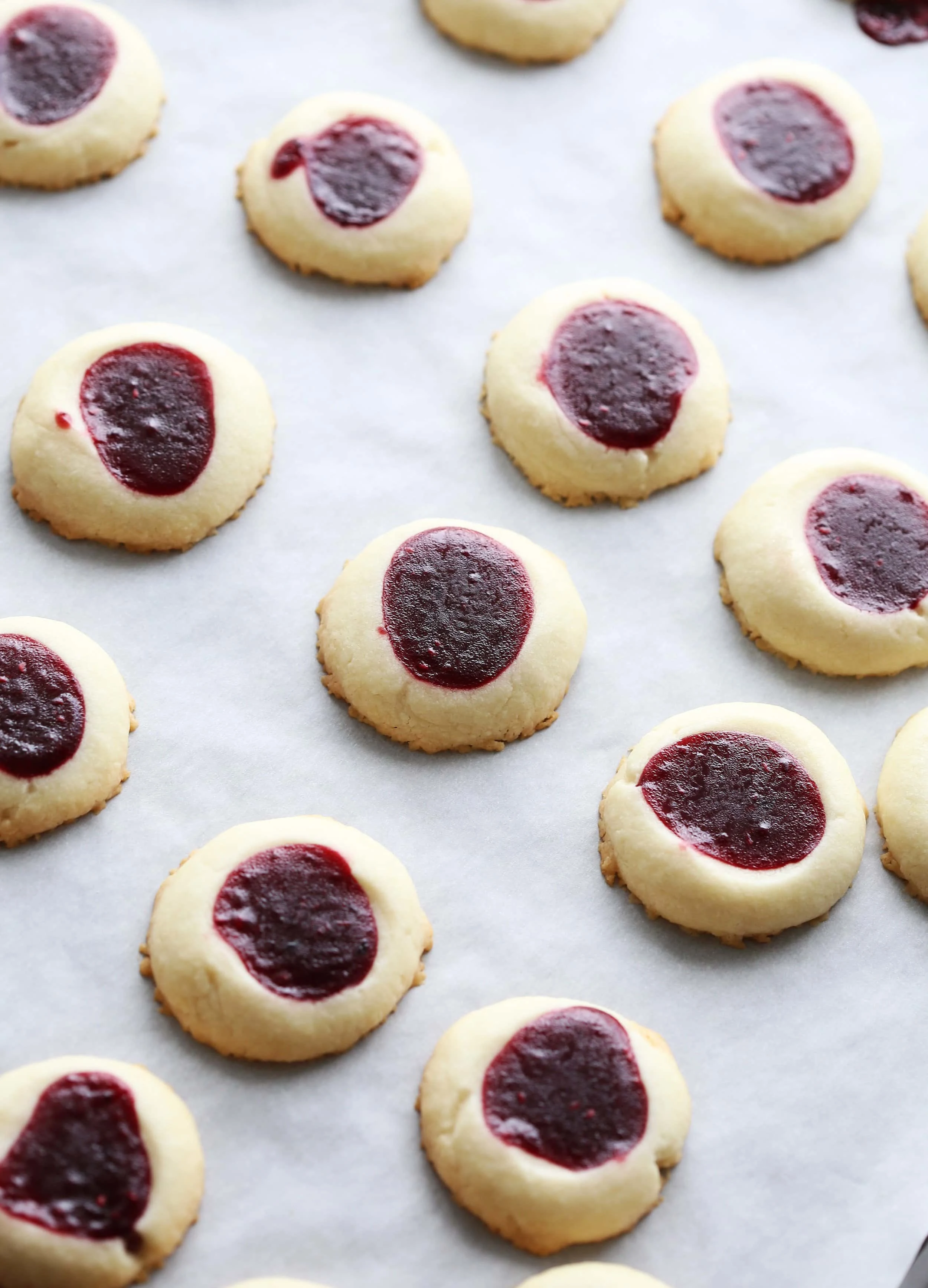 Baked raspberry shortbread thumbprint cookies on a baking sheet.