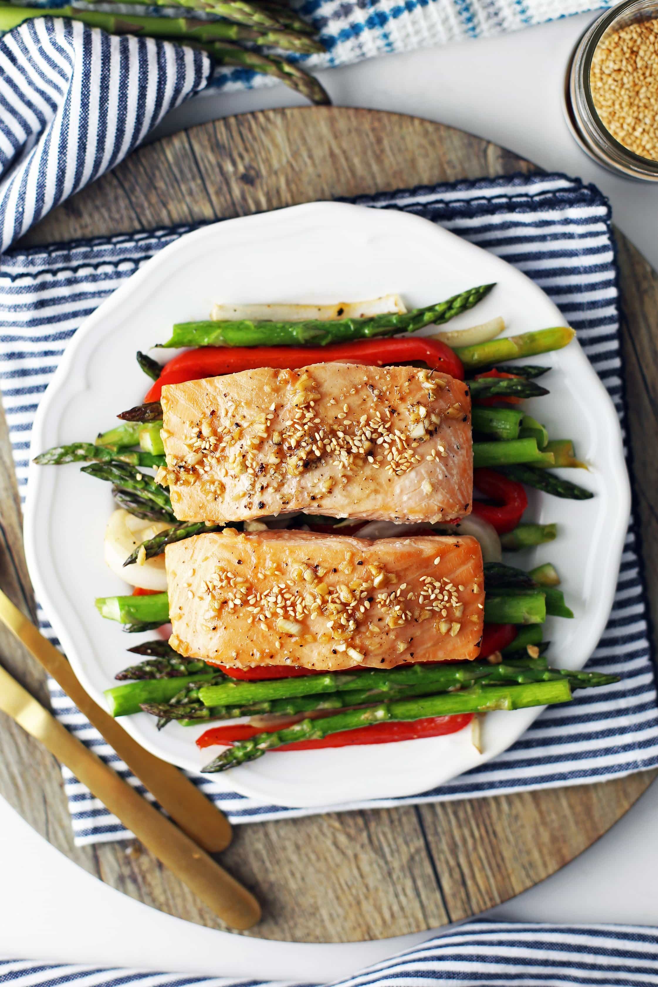 Overhead view of two baked salmon fillets on a bed of roasted asparagus, bell pepper, and onions on a white plate.