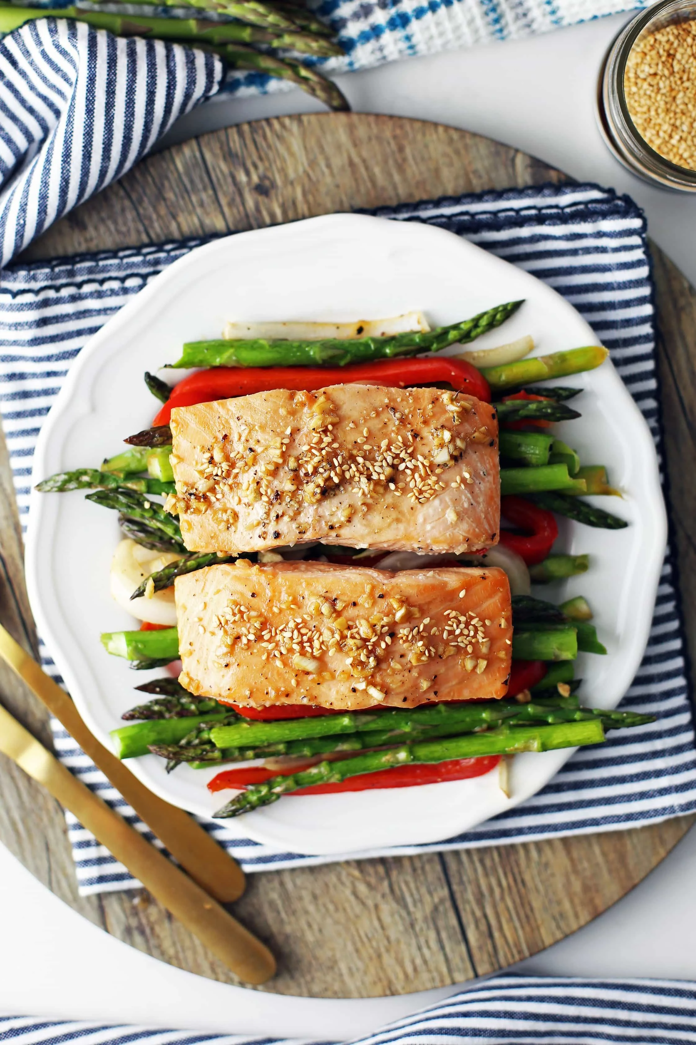 Overhead view of two baked salmon fillets on a bed of roasted asparagus, bell pepper, and onions on a white plate.