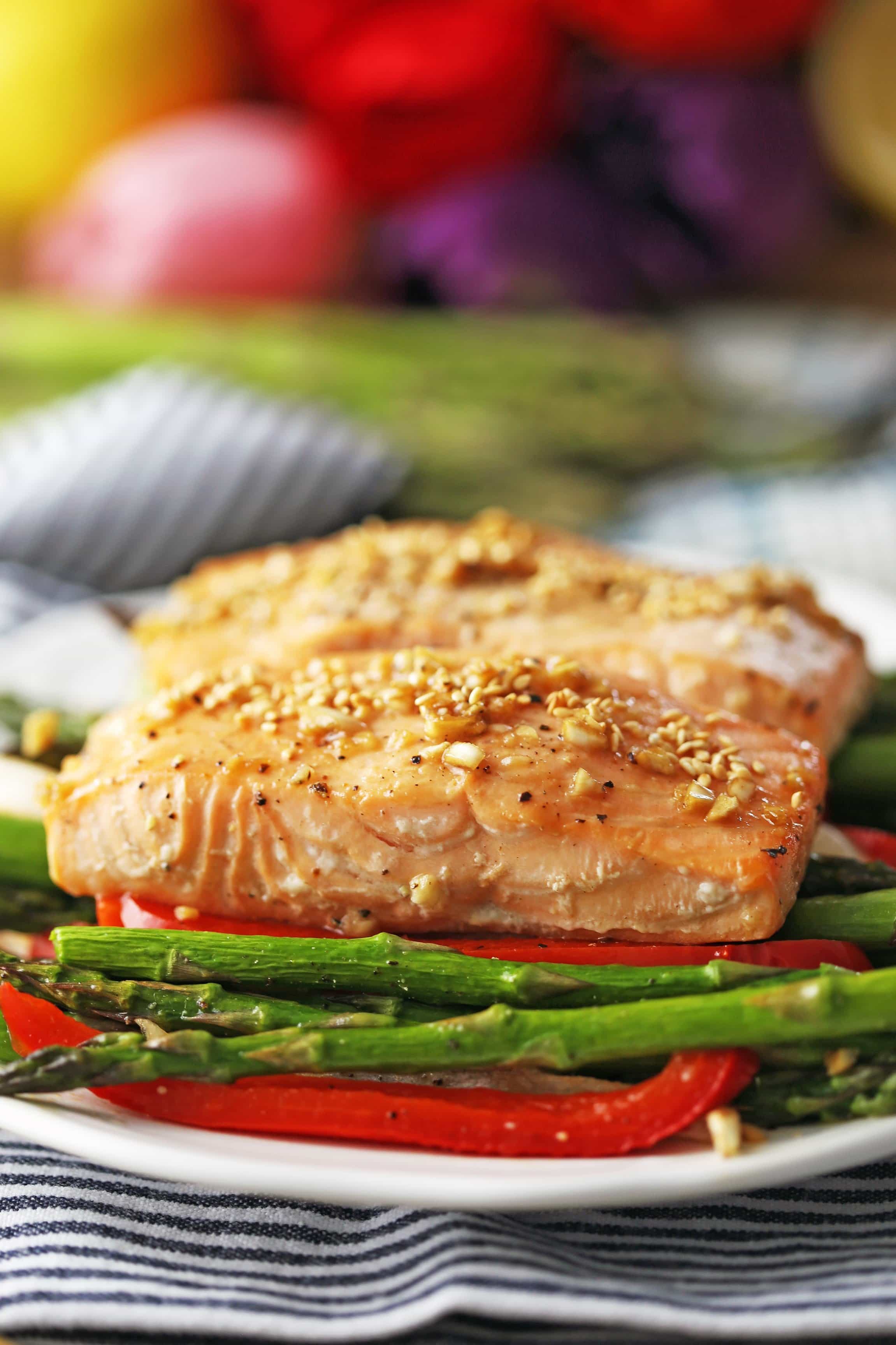 Side view of baked salmon with roasted asparagus, bell peppers, onions on a white plate.