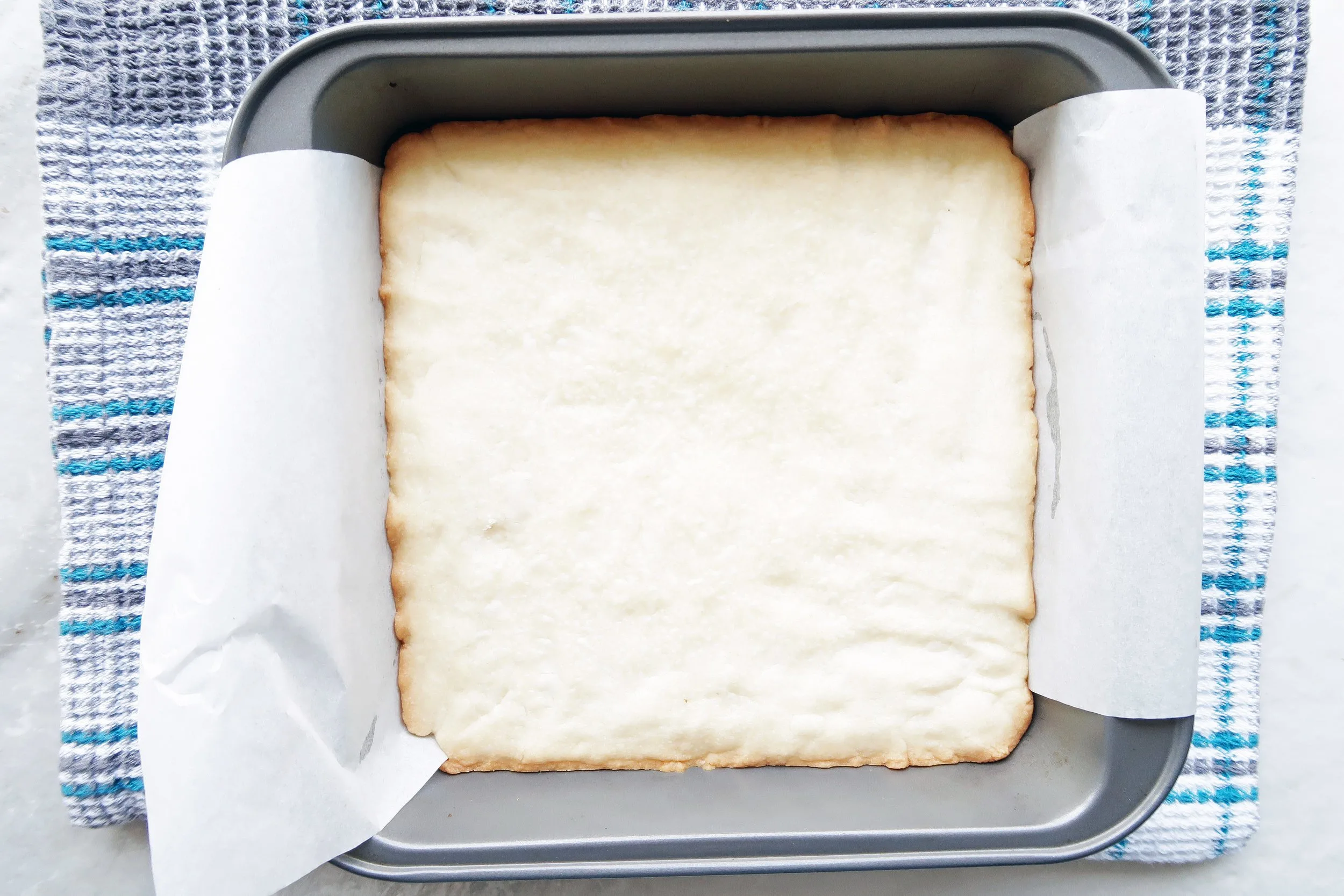 Baked shortbread in a parchment paper-lined square baking pan.