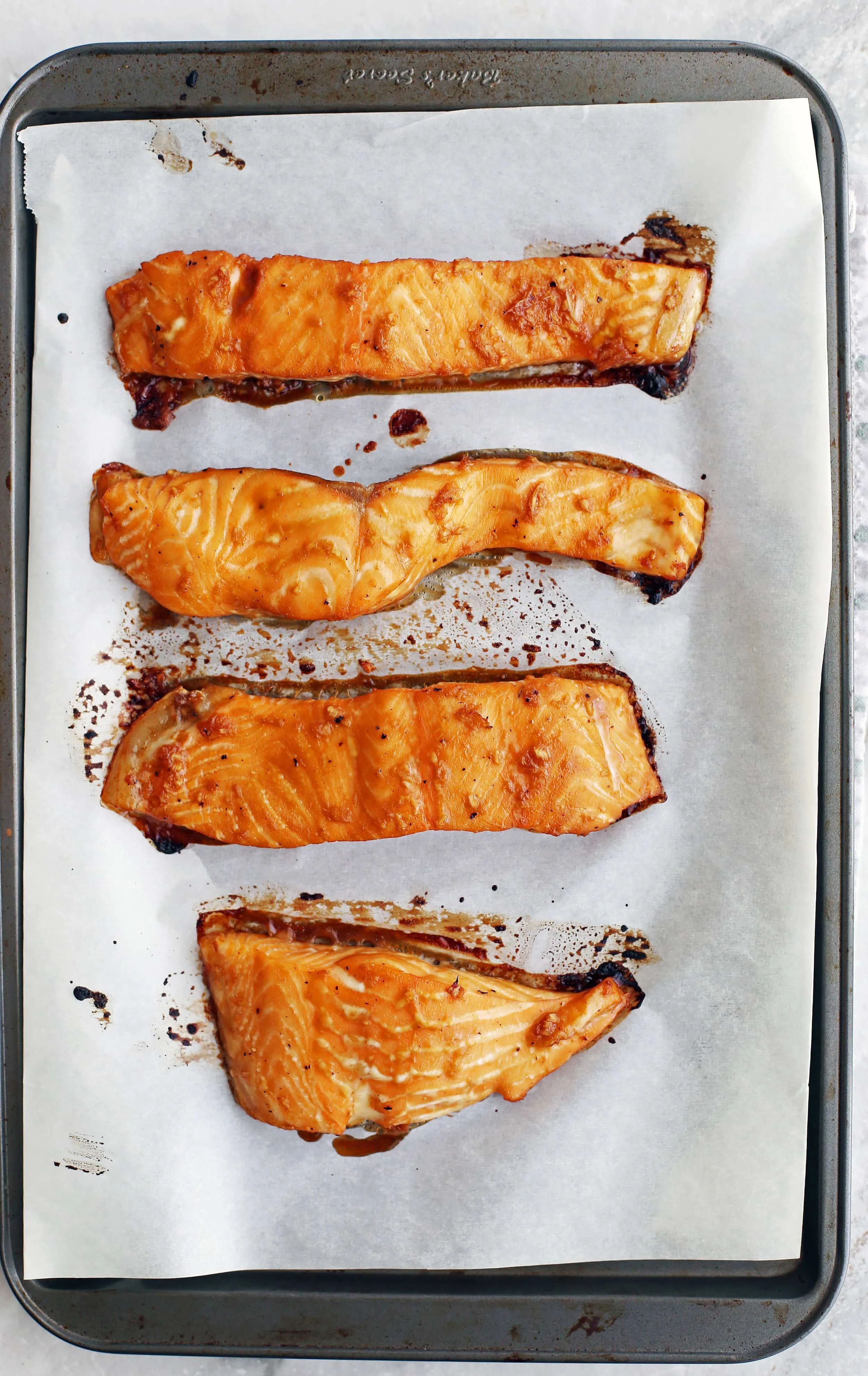 Four maple-soy baked salmon fillets on a baking sheet.