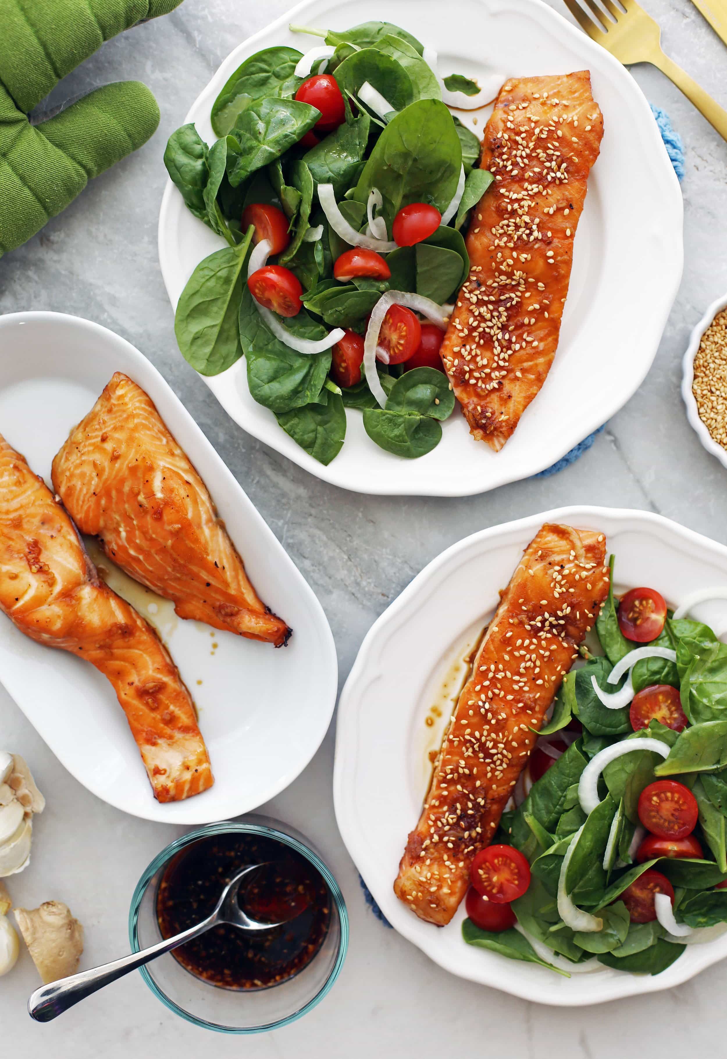 Overhead view of three white plates containing maple-soy baked salmon and spinach salad.