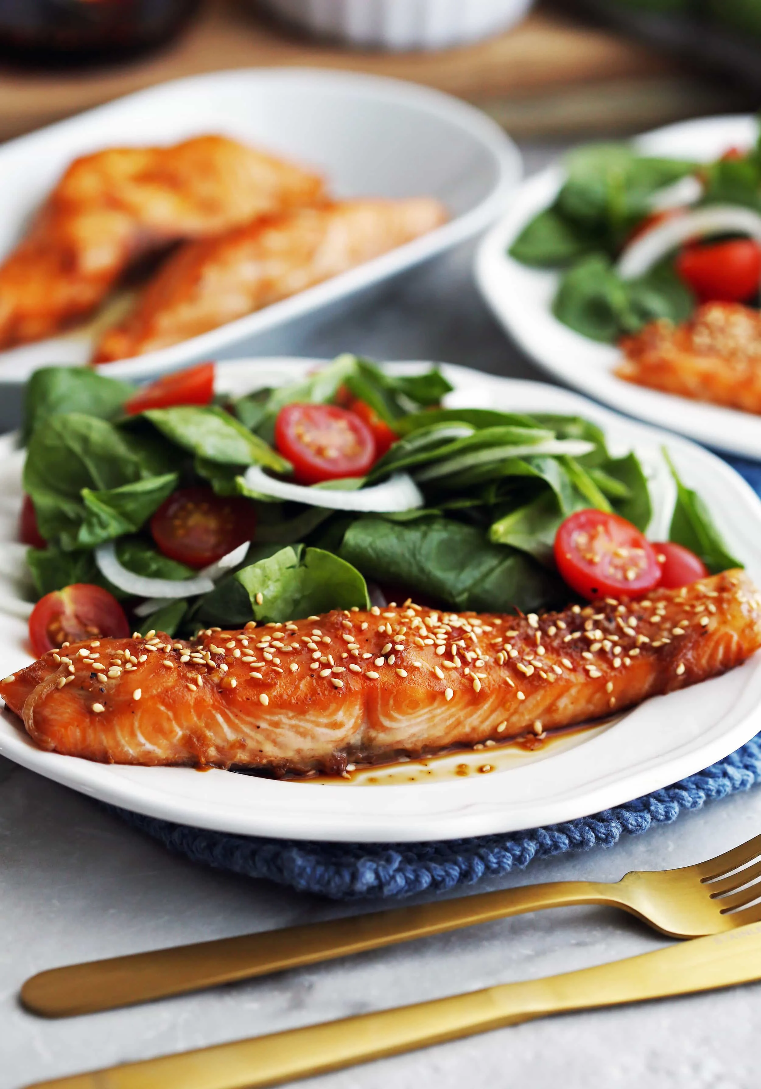 Maple-Soy Baked Salmon topped with sesame seeds with green spinach salad on a white plate.