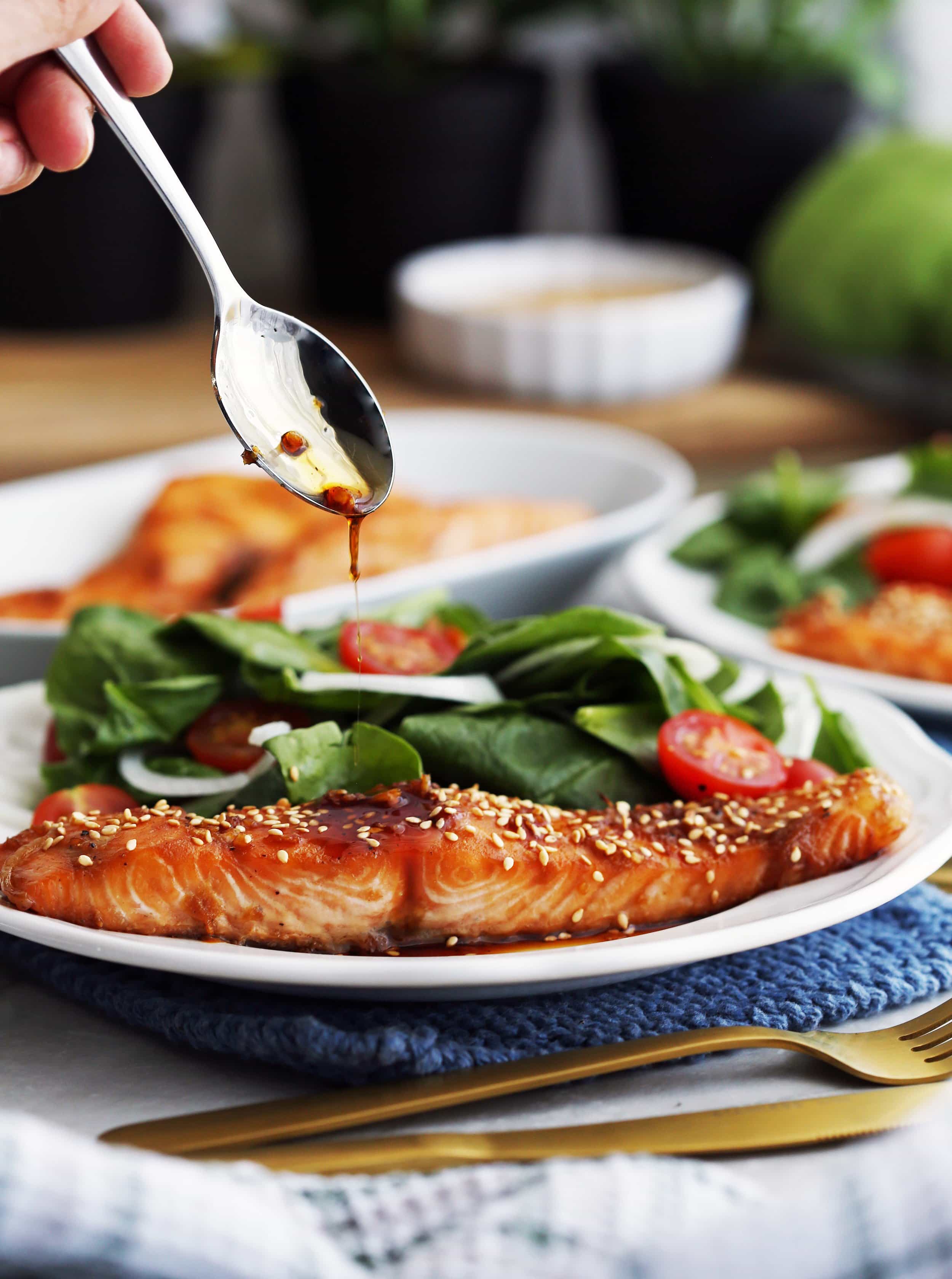 Maple-soy baked salmon on a white plate topped with a spoonful of maple-soy sauce.