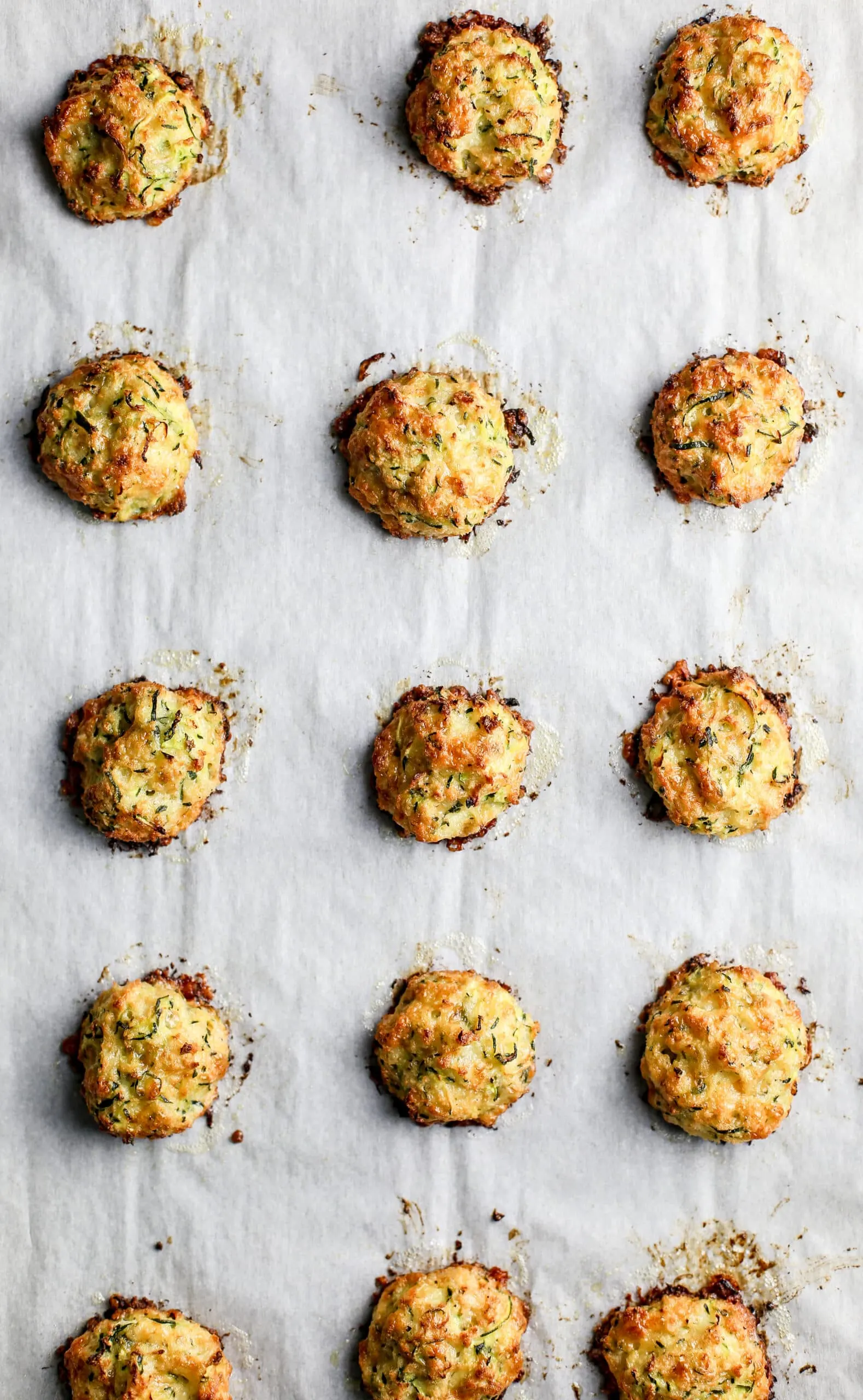 Baked zucchini bites on top of a parchment paper lined baking sheet.