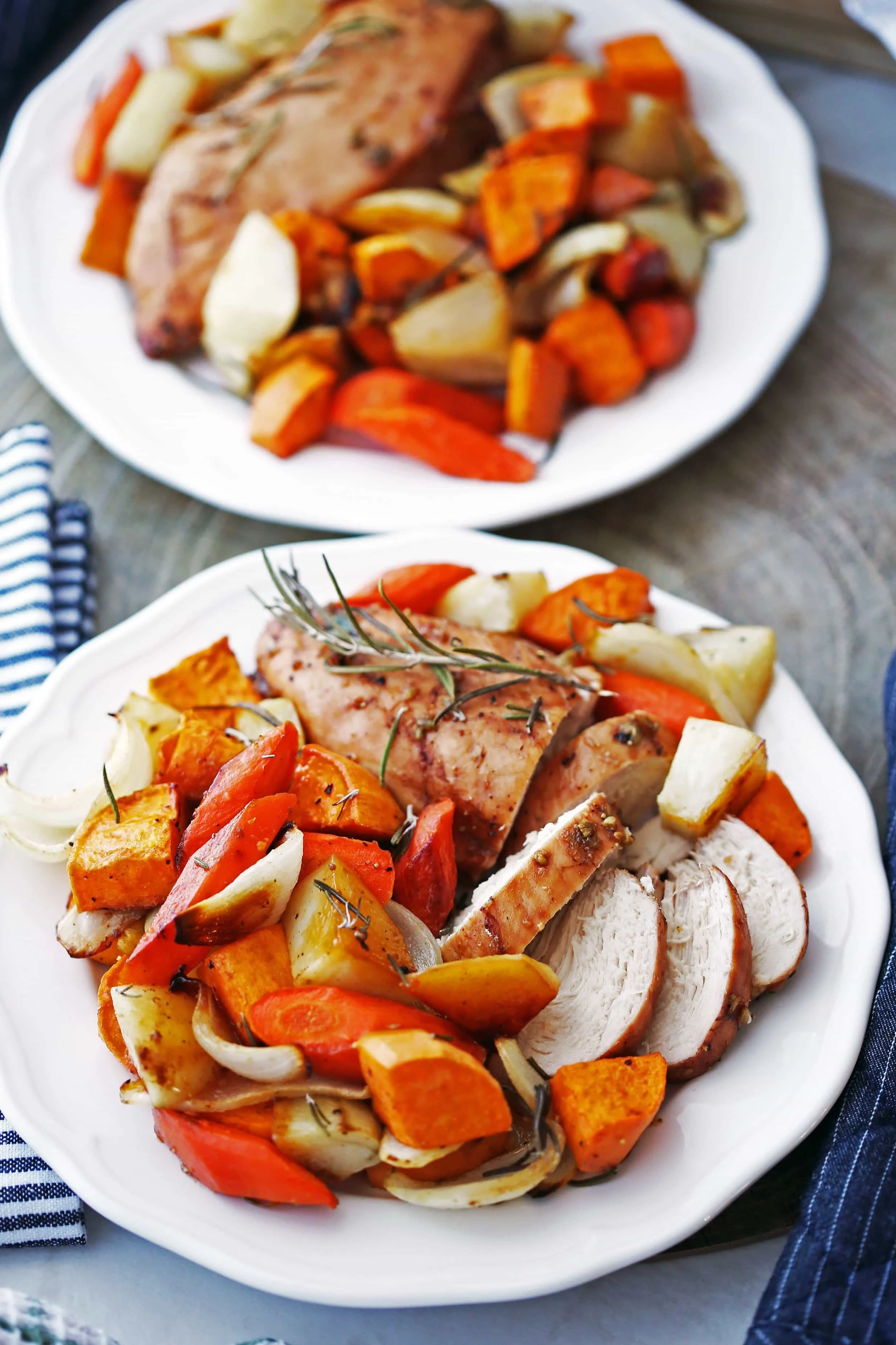 Two white plates containing baked balsamic chicken breasts and roasted vegetables, including potatoes and carrots.