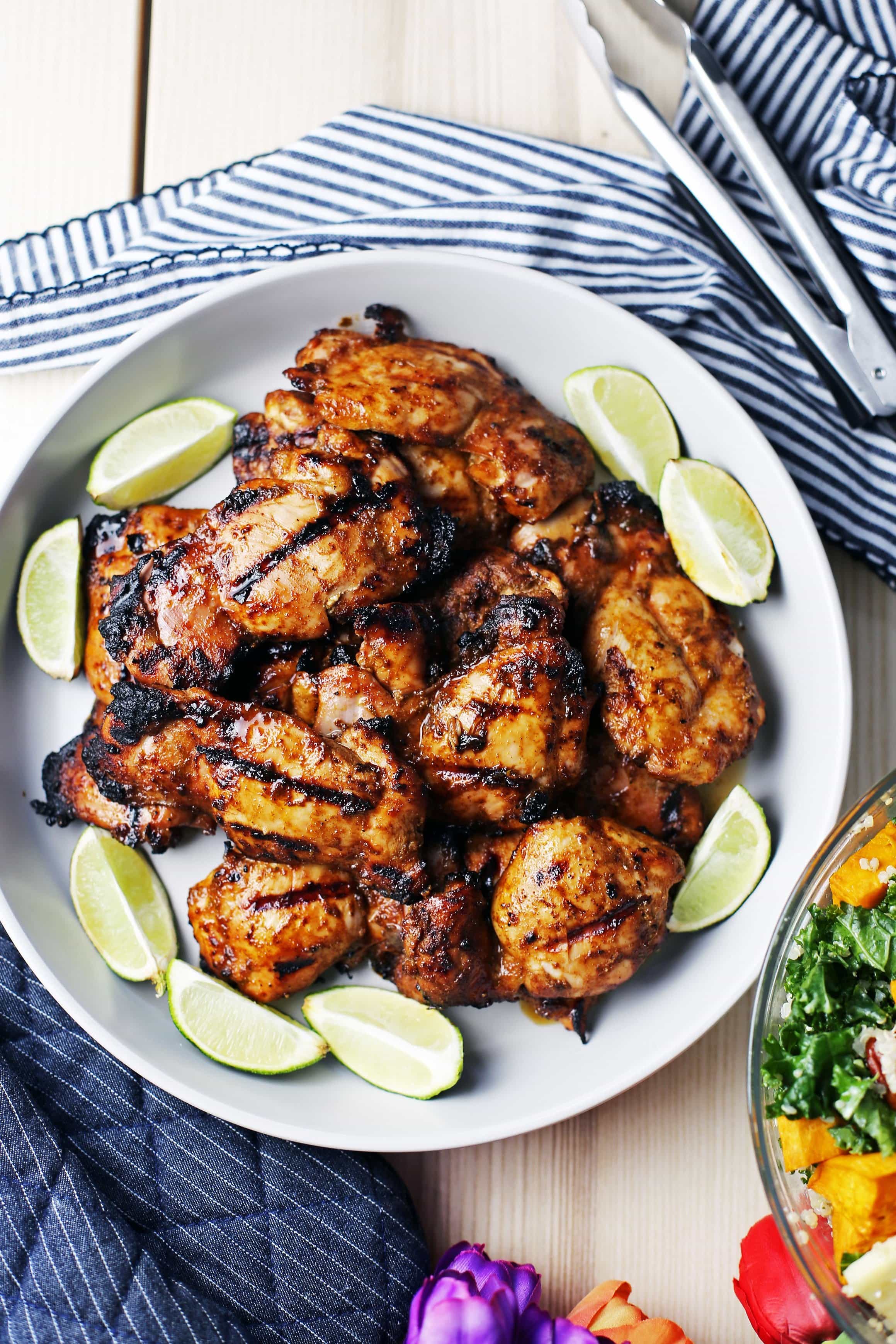 Overhead view of a large grey round platter containing a dozen grilled chili lime chicken thighs.